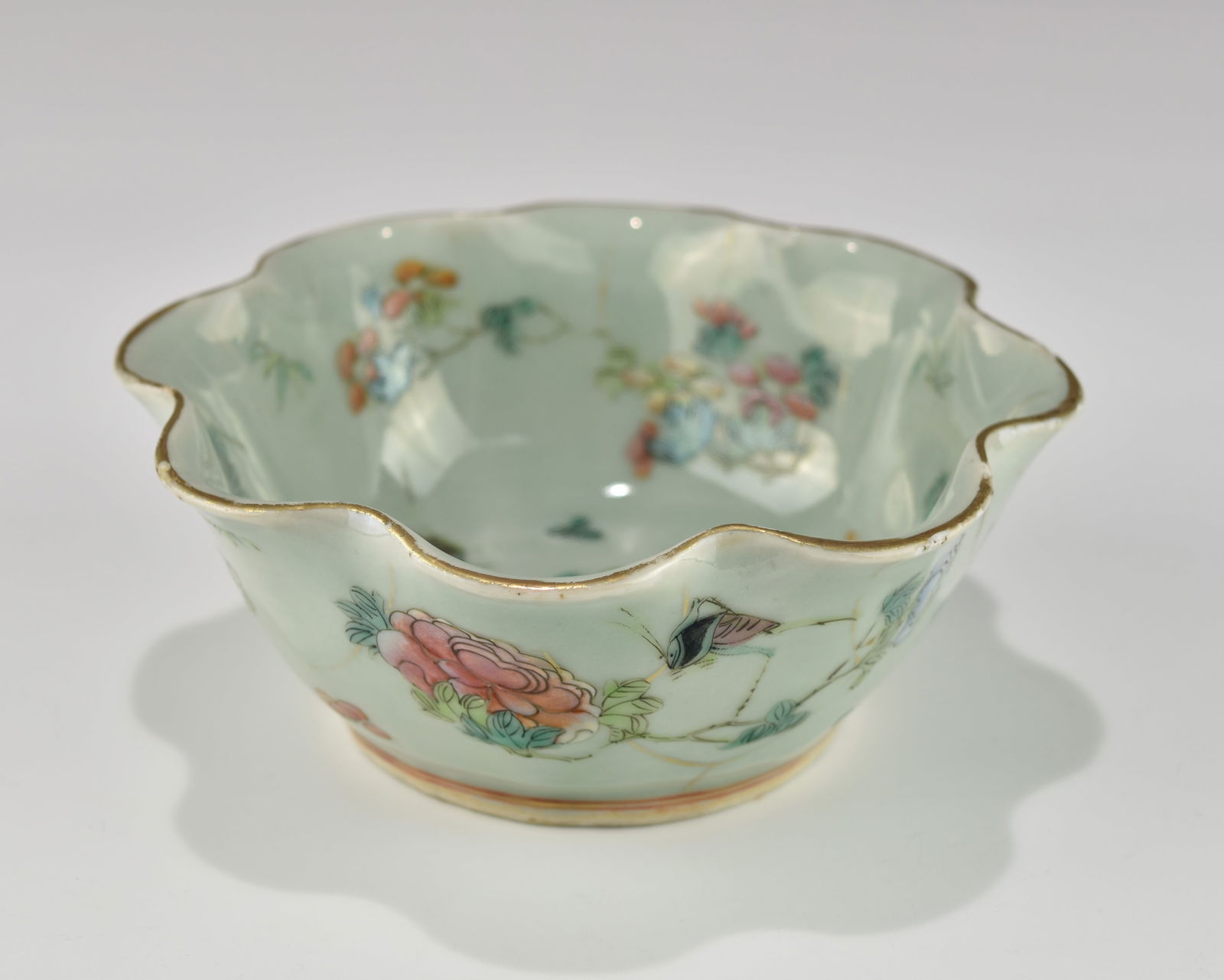 A CHINESE QING TONGZHI FAMILLE ROSE SCALLOP CELADON GLAZE PORCELAIN BOWL: 19TH century, with both interior and exterior of the bowl decorated with flowers and insects in famille rose enamels, gilt top rim. An iron-red six-character Tongzhi mark to the base, in overall good