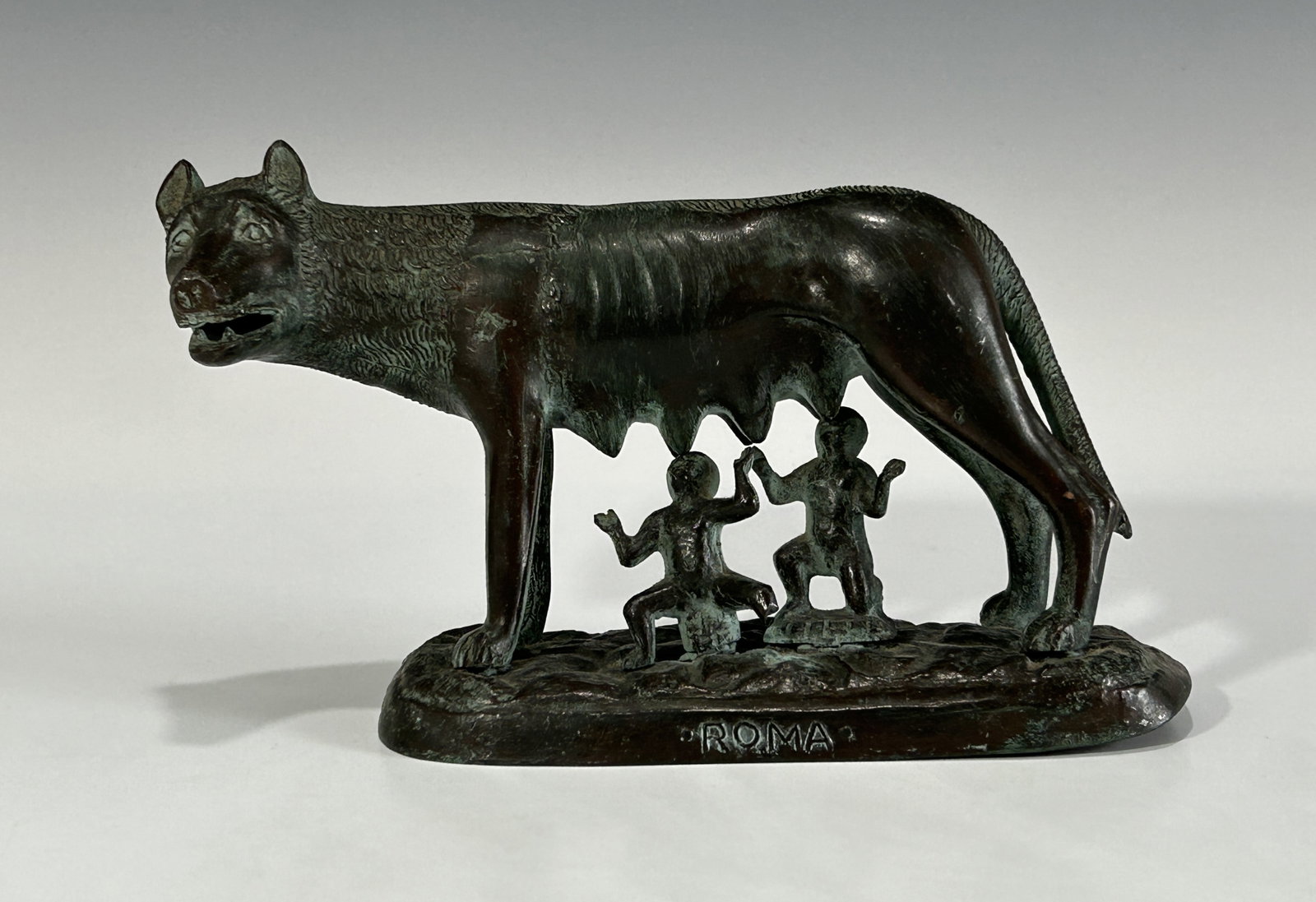 AN ANTIQUE BRONZE STATUE, LUPA CAPITOLINA SHE-WOLF WITH ROMULUS AND REMUS: Circa 1920s. The mother wolf is in a standing position with Romulus and Remus under beneath, all resting on a bronze slab with "ROMA" engraved at the front. In overall good antique condition with nice