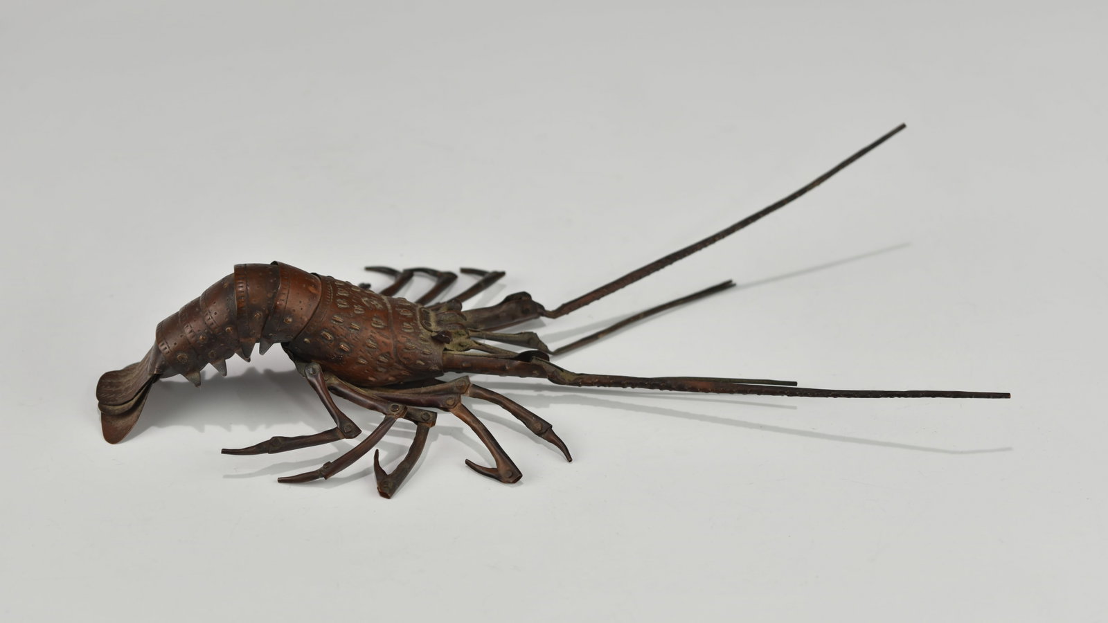 AN JAPANESE MEIJI PERIOD ARTICULATED OKIMONO LOBSTER BY HIROYOSHI MYOCHIN: Circa 1890, artist signed on the underside. This lobster was fully articulated in life-size with copper or a copper alloy in a realistic fashion with meticulous details from the antennas, body, joins,