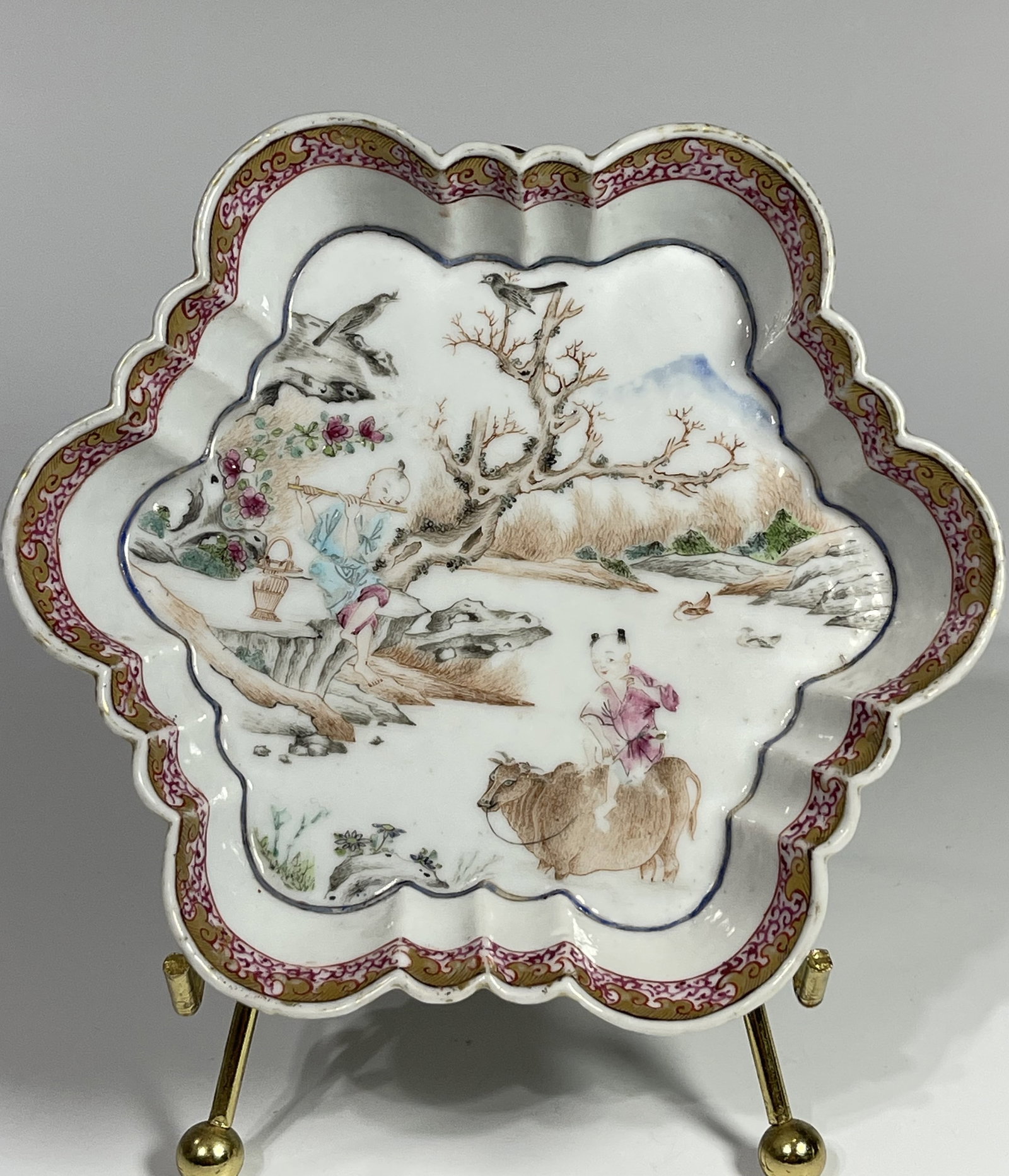 A CHINESE QING DYNASTY QIANLONG HEXAGONAL FLUTED PORCELAIN DISH: 18th century, depicting one boy sit on the back of a buffalo, and another boy sitting nearby on rock playing flute with feet dangling, in a traditional Chinese landscape view. In good condition with s