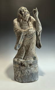 ANTIQUE CHINESE CARVED WOODEN LOHAN STATUE, MING DYNASTY OR EARLIER: An impressive and expressive Chinese carved wooden figure of a Lohan (Arhat), dating to the Ming Dynasty, 14th–15th century, or possibly earlier. The Lohan is depicted standing barefoot atop a circu