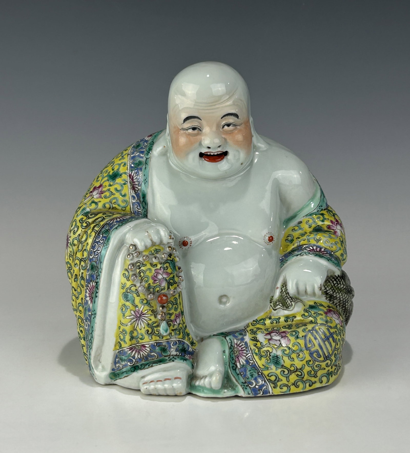 ANTIQUE 19TH CENTURY CHINESE FAMILLE ROSE PORCELAIN LAUGHING BUDDHA: Finely modeled, dating from the late Qing Dynasty to the Republic Period, depicted in a traditional seated posture with a corpulent belly exposed, symbolizing abundance and happiness. The Buddha's fac