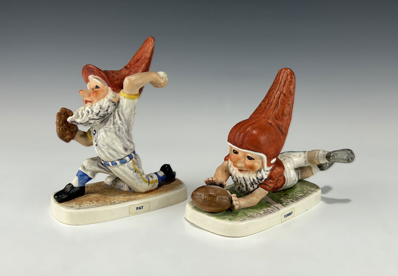 PAIR OF GOEBEL WEST GERMANY GNOME PORCELAIN FIGURINES, “PAT?? AND “TOMMY: A whimsical pair of vintage porcelain figurines by Goebel, West Germany, depicting playful gnomes engaged in sports. One, titled “Pat,” portrays a baseball pitcher mid-throw with glove and bal