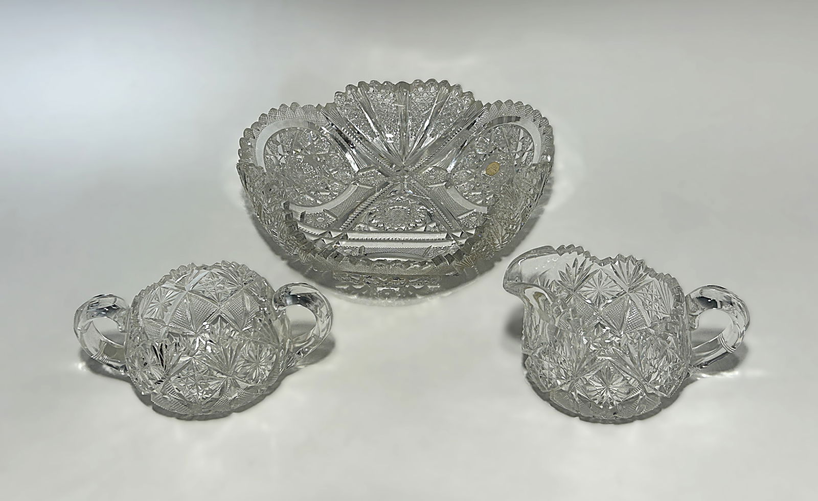 AMERICAN BRILLIANT PERIOD STRAWBERRY CUT GLASS THREE-PIECE SET: American Brilliant Period strawberry cut glass three-piece set, including bowl, creamer, and double-handled sugar, circa 1890. Finely cut with dense strawberry, hobstar, fan, and starburst motifs; sca
