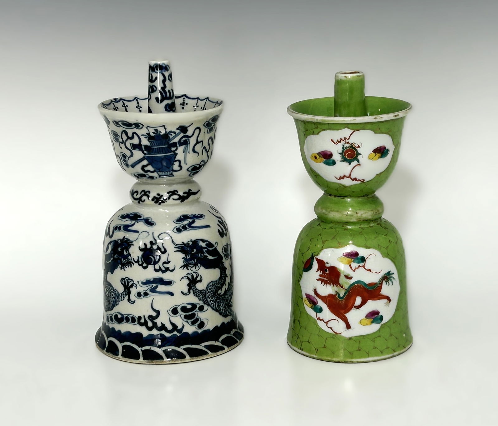 TWO CHINESE PORCELAIN JOSS STICK CANDLESTICKS OR OIL LAMPS: 19th to 20th century, of traditional bell form with a stepped, waisted neck and wide flared drip pans, including one blue and white example featuring a pair of five-clawed imperial dragons pursuing th
