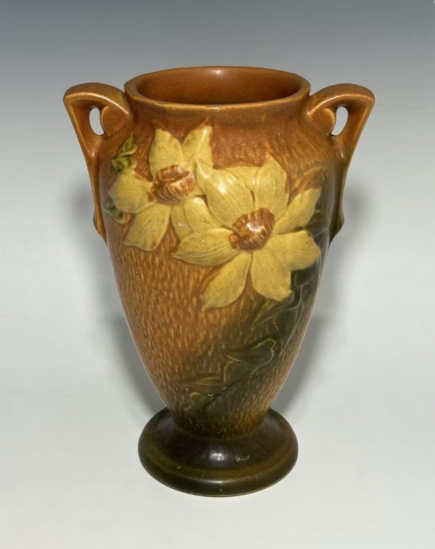 VINTAGE ROSEVILLE POTTERY “CLEMATIS?? VASE, CIRCA 1940S: The vase is formed in an urn-shaped silhouette with a flared rim, rounded body, and a molded pedestal foot, fitted with two opposing angular loop handles at the shoulder. Decorated in the Autumn Brown