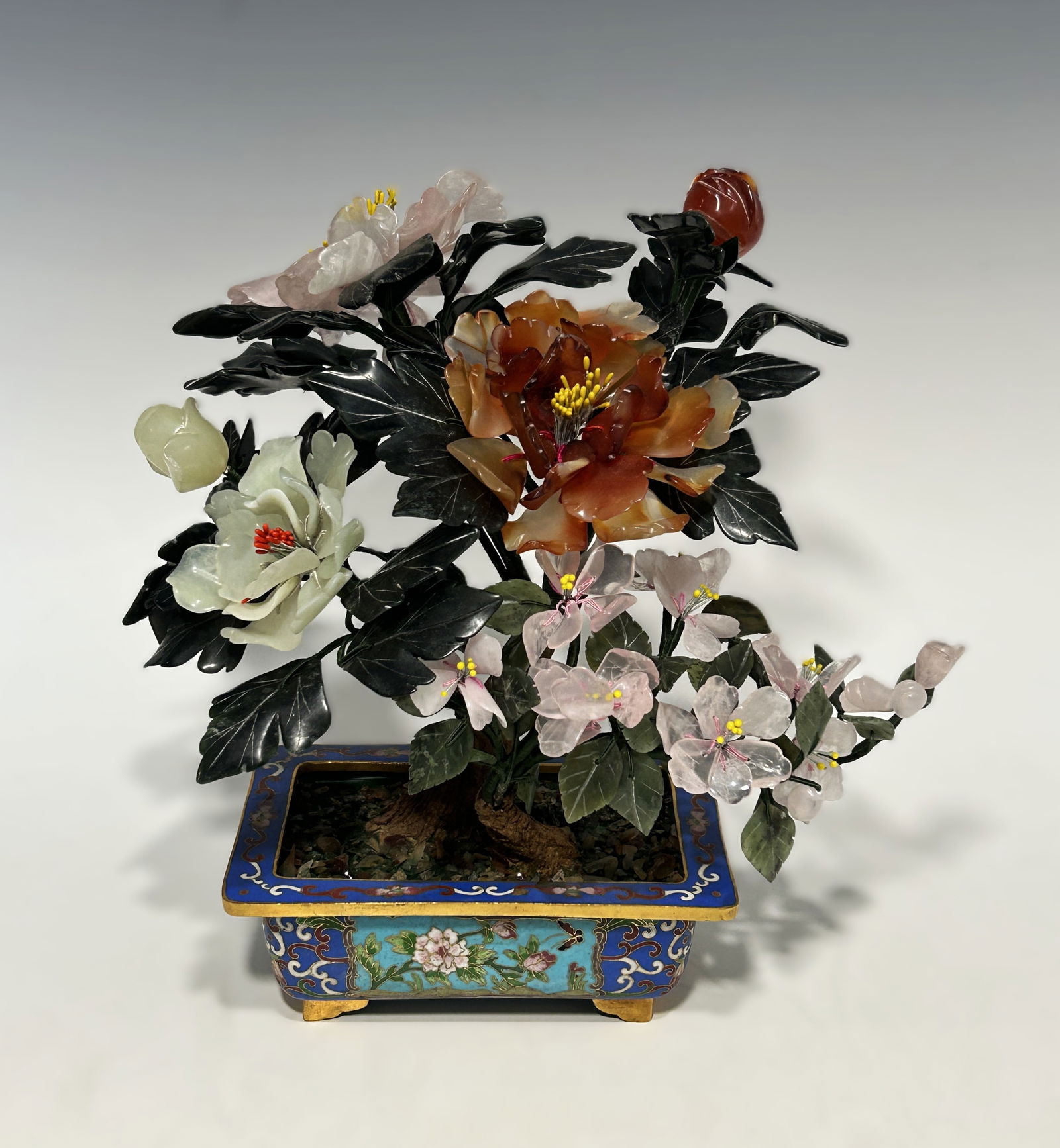 CHINESE CARVED JADE AND HARDSTONE BONSAI TREE: Republic Period/Early 20th Century, featuring a naturalistic trunk supporting an array of vibrant, hand-carved semi-precious stone blossoms. The arrangement includes large peony flowers in hues of var