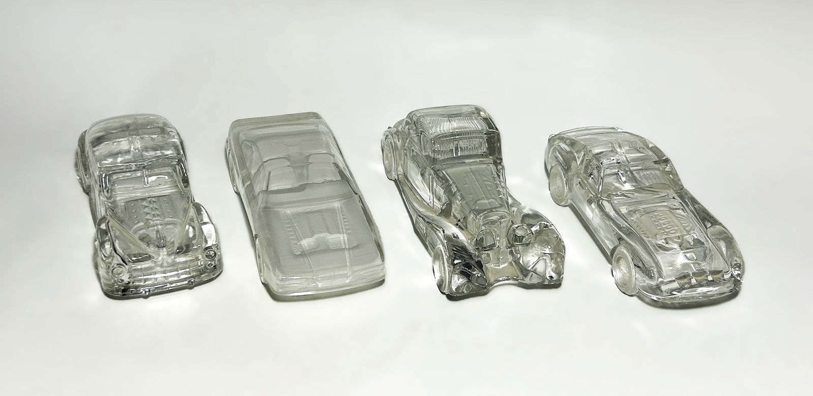 COLLECTION OF FOUR VINTAGE CRYSTAL AND ART GLASS AUTOMOTIVE PAPERWEIGHTS: A diverse grouping of four clear and molded glass automotive-themed paperweights and sculptures. This collection represents a span of 20th-century glass manufacturing, from mid-century American novelt