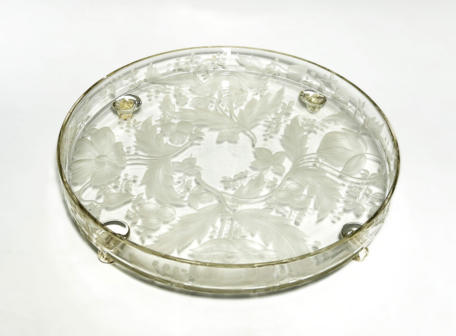LARGE MID-CENTURY ETCHED AND FROSTED GLASS FOOTED SERVING PLATTER: Elevated on four integrated scroll-form feet, decorated with intaglio-etched and frosted spray of floral motif. The interior surface remains smooth and polished, while the exterior provides a tactile,