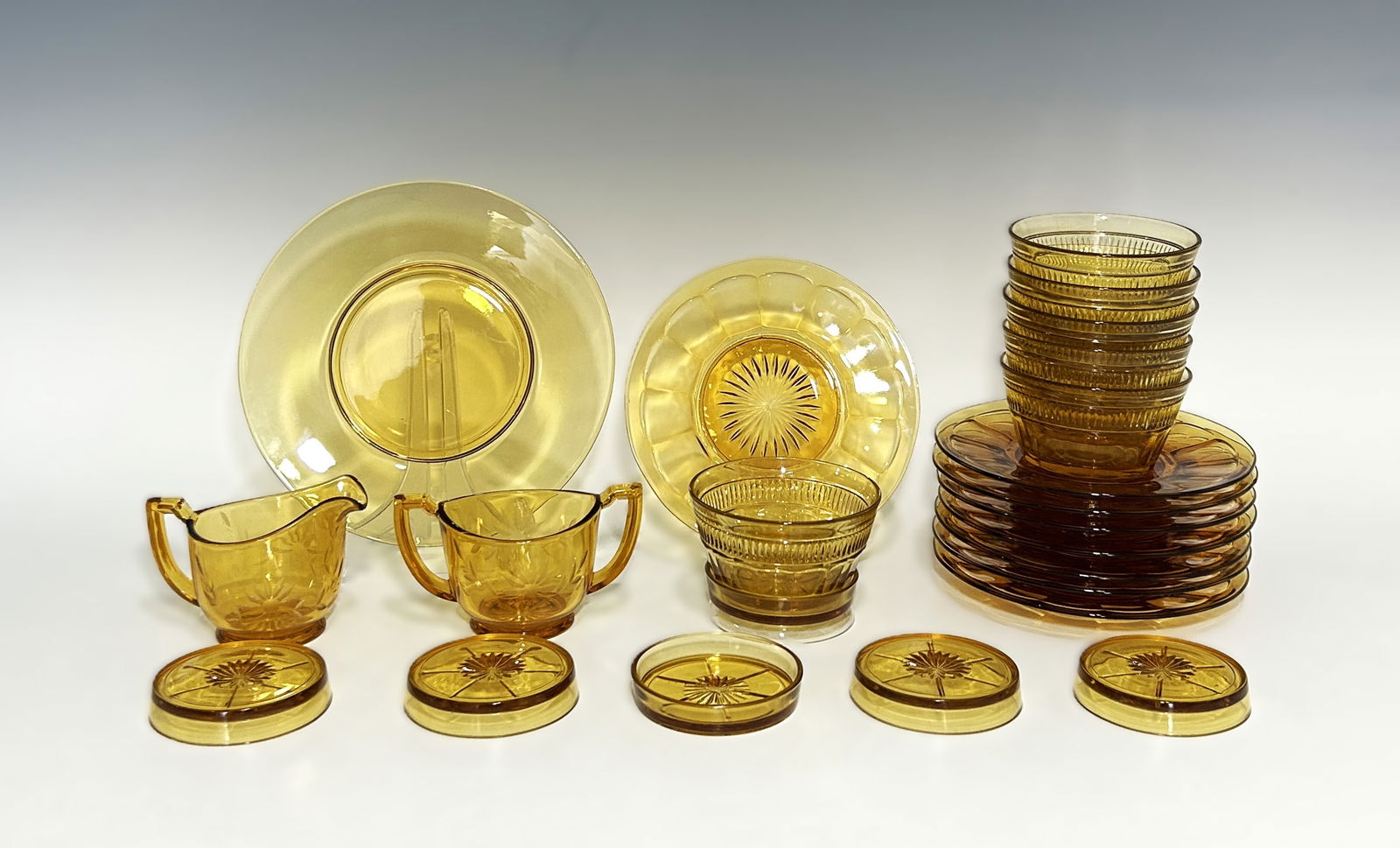 21 PIECE VINTAGE DEPRESSION-ERA DAISY PATTERN AMBER GLASS DINNERWARE SET: Circa 1940s, featuring a mix of functional tabletop items with detailed molded patterns. The collection is highlighted by a "Daisy" floral and starburst motif, a hallmark of mid-century American depre