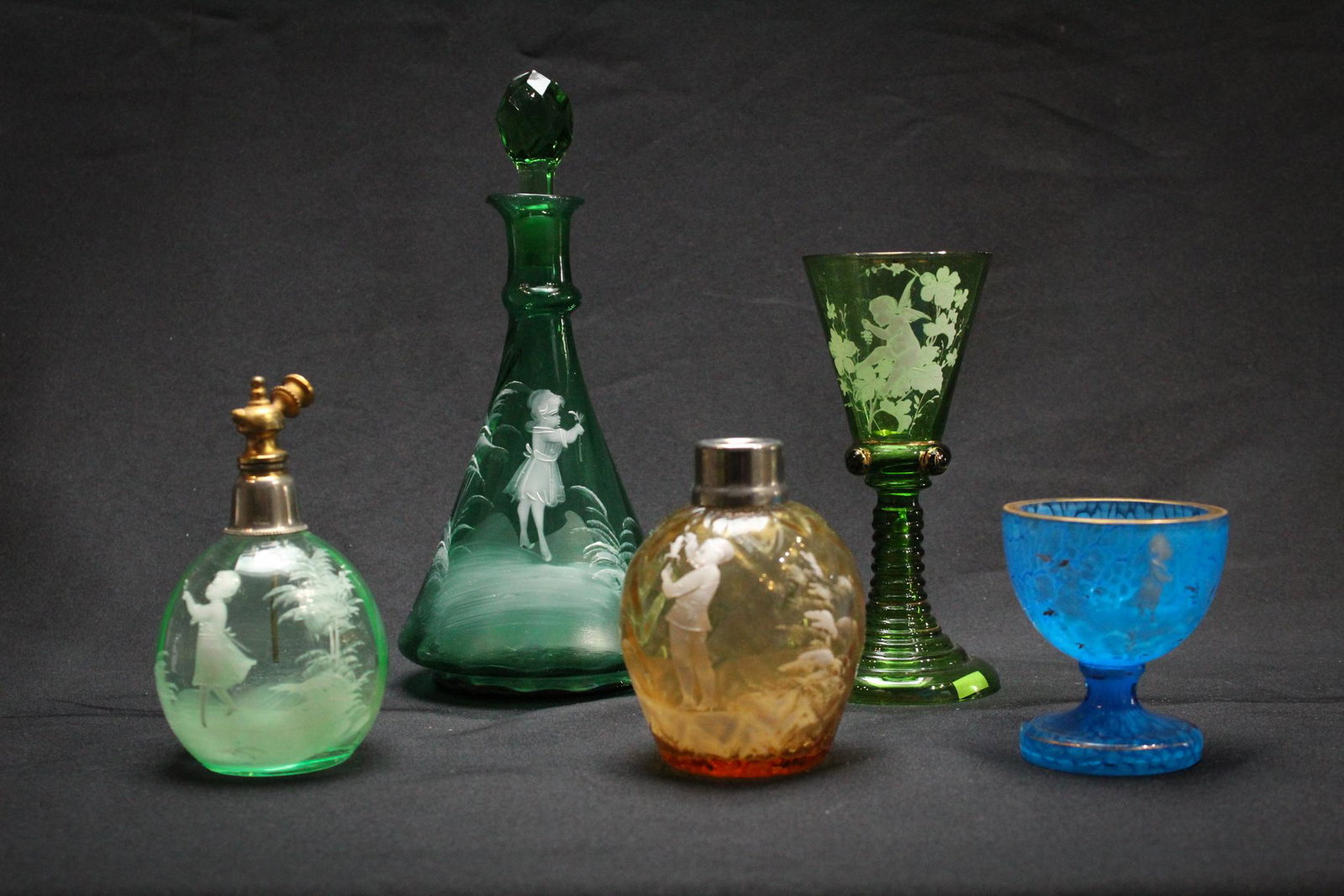 5 pcs of Mary Gregory Victorian glass: A wonderful lot of 5 pieces of Victorian Mary Gregory glass to include a 2 atomizers, a cologne bottle, a custard cup, and a wine. Tallest measures 9", 4"wide. Condition: Excellent