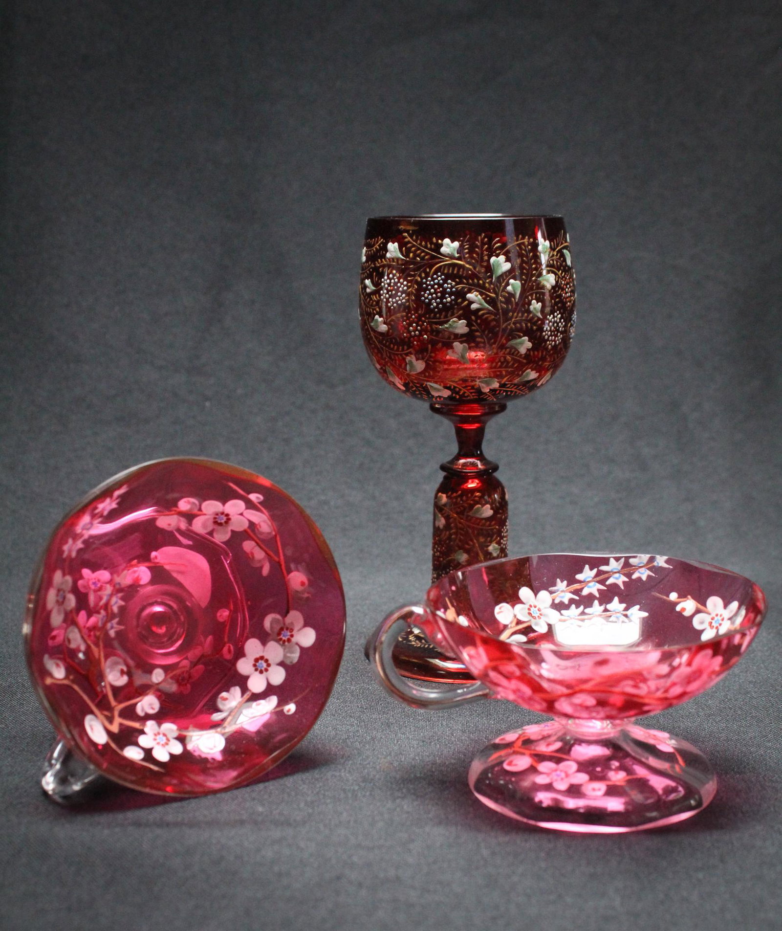 Lot 3 pcs. Victorian Cranberry Enameld Glass incl.: A beautiful lot of 3 pieces of Victorian Cranberry glass to include 2 pedestal foot punch cups and a wine goblet. Latter attributed to Moser. Tallest measures:5 1/2", 2 1/2" wide. Condition: Excellent