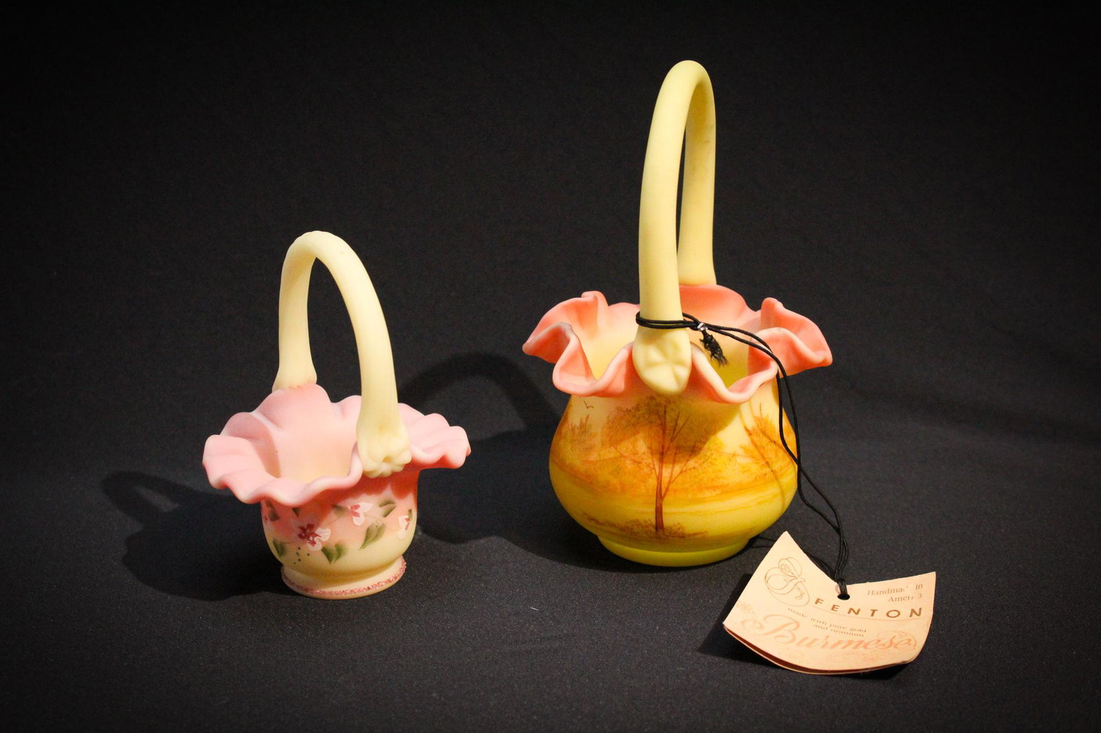 Lot of 2 Fenton Glass Burmese baskets: Lot of 2 Fenton Glass Burmese baskets to include a miniature. Tallest measures 6 1/4" tall.