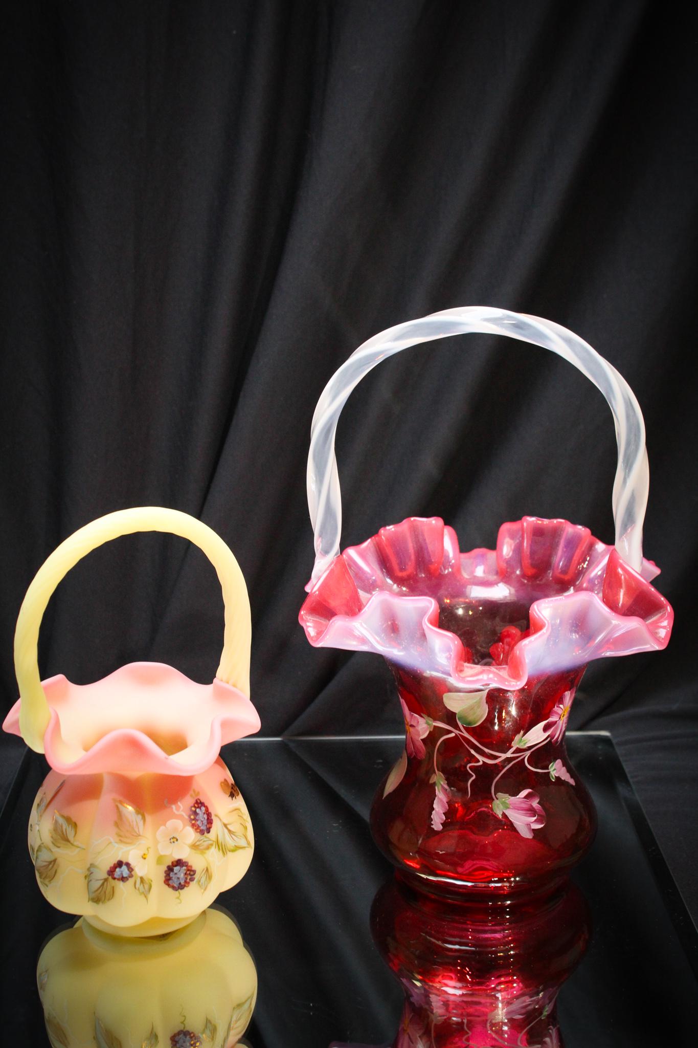 2 pc Lot Fenton Glass Hand Painted Baskets: Here we have a 2 piece lot of Fenton glass baskets comprised of a cranberry opalescent and a burmese example. Both are hand painted. Tallest measures 10 1/2" tall.