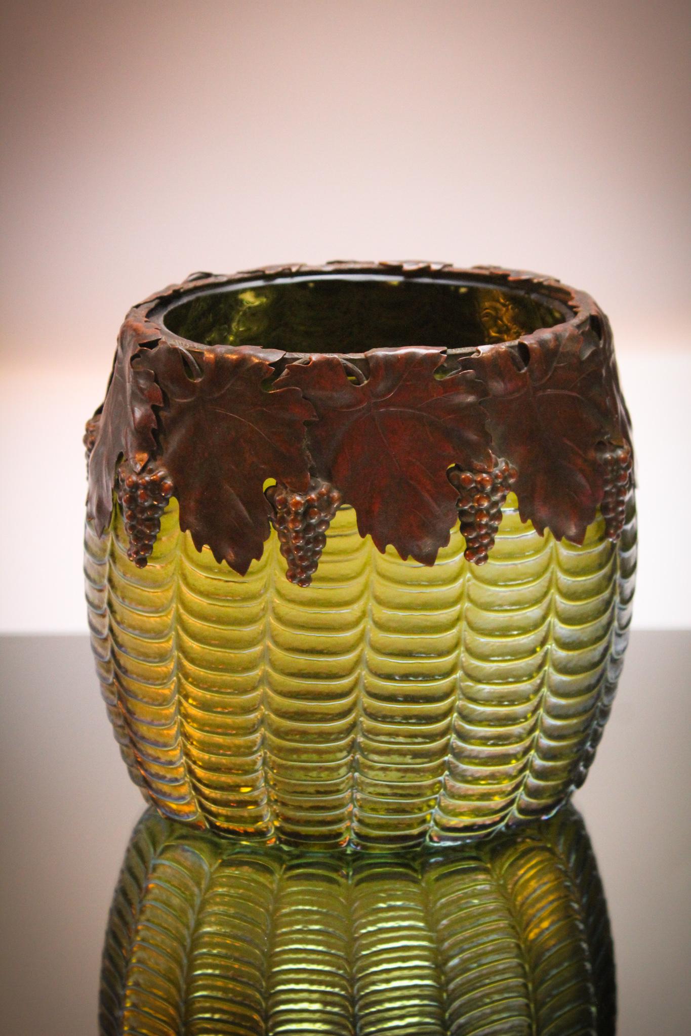 Wilhelm Kralik Drape Green & Metal Mounts Vase: You'll be green with envy if you don't win this pretty piece. Wilhelm Kralik glass drape pattern pillow vase with a grape embossed metal collar. Nice color and iridescence. Measures 6 1/2" tall.