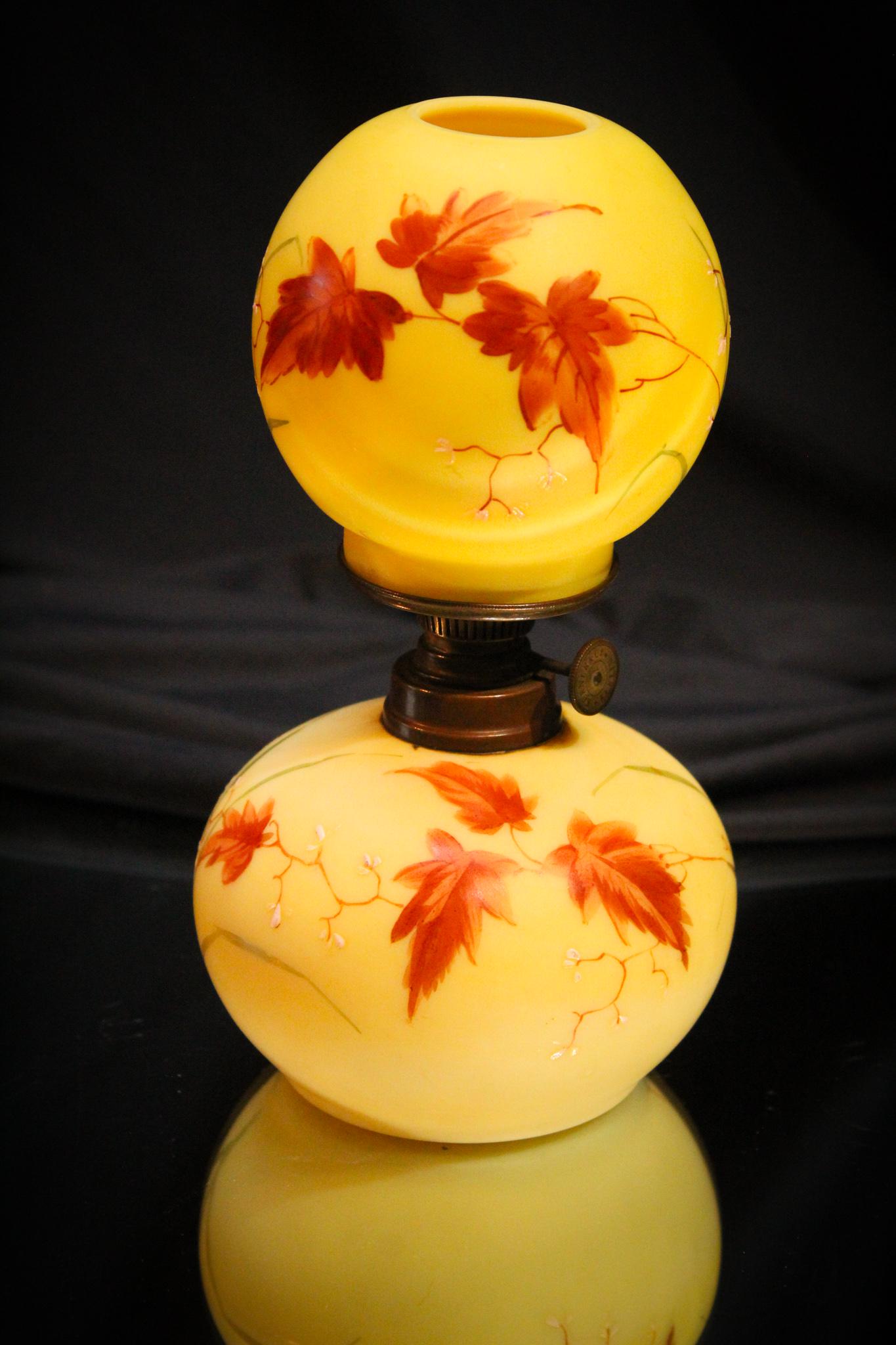 Victorian Yellow Satin Enameled Miniature Oil Lamp: An abundance of foliage decorates this super miniature oil lamp in yellow satin. Lamp is compplete with original Kosmos burner and original shade. Great example. Measures 7 1/2" tall.