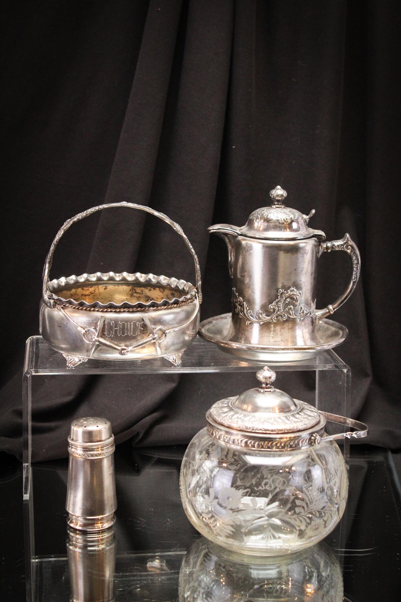 4 pc Pairpoint Silverplate Lot: Select offering of four pieces of Pairpoint silverplate comprised by a basket, a creamer with underplate, a salt shaker, and finally an engraved glass sweetmeat. Tallest measures 5".