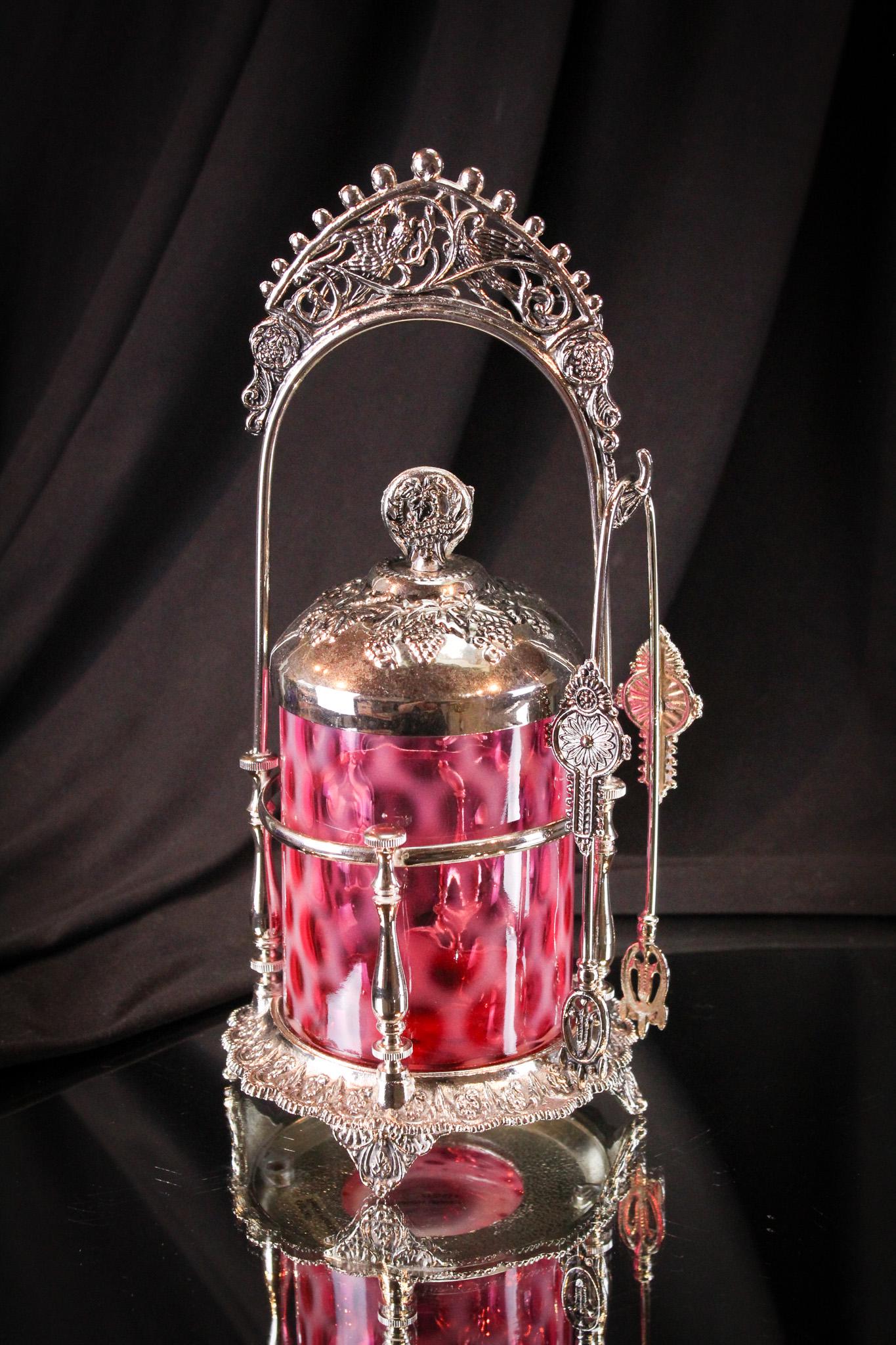 Fenton L G Wright Cranberry Opalescent Honeycomb Pickle Castor: Striking cranberry is the color of this opalescent pickle castor jar made by Fenton for L.G. Wright. Complete in original frame, it stands a proud 10 1/2" tall.