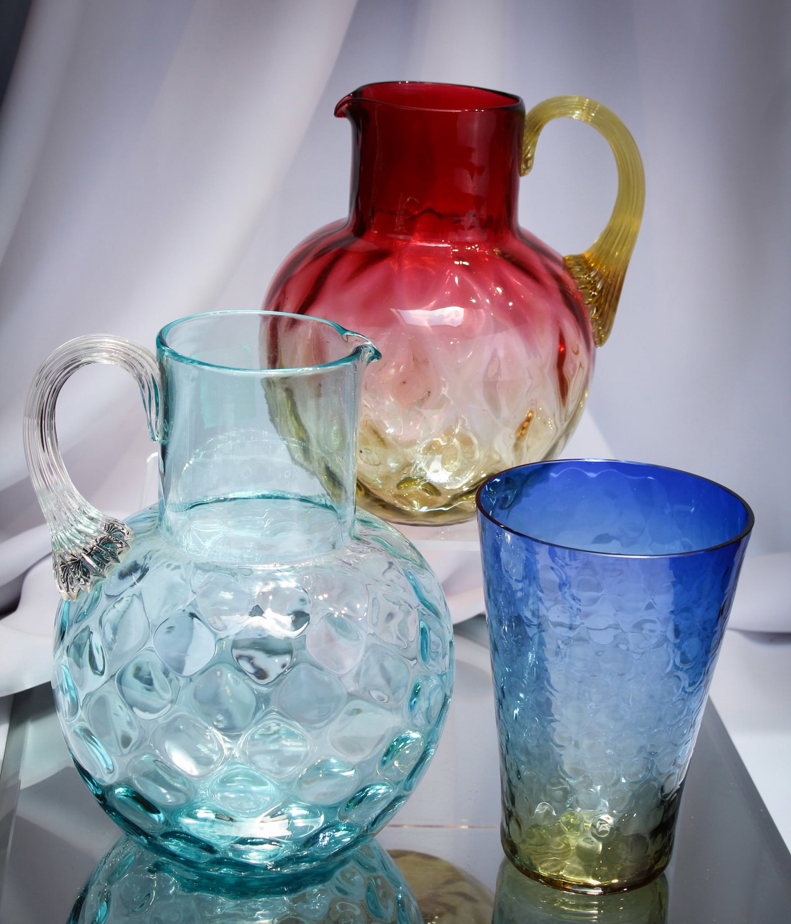 3 pc Lot Victorian & More Art Glass: Select offering of three pieces of art glass. An amberina Victorian diamond quilt water pitcher, a blue inverted thumbprint Victorian pitcher and a bluerina more recent vase of continental origin.