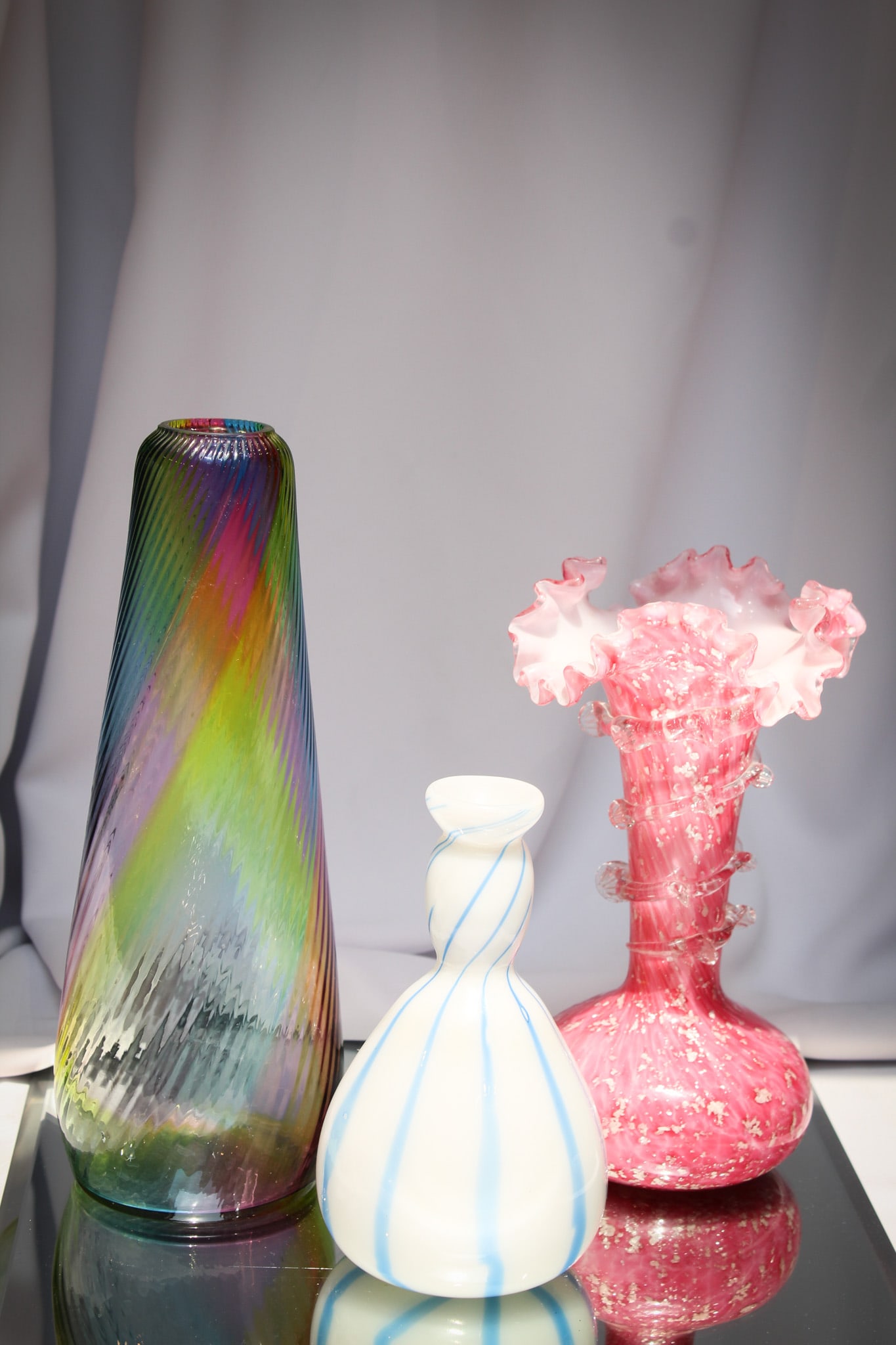 3 pc Lot Victorian Glass & More Rainbow Spangle: Hand selected offering of three fine pieces of art glass comprised by a Victorian Rainbow swirled vase, a spangle pink cased with rigaree vase, and an italian bottle vase.