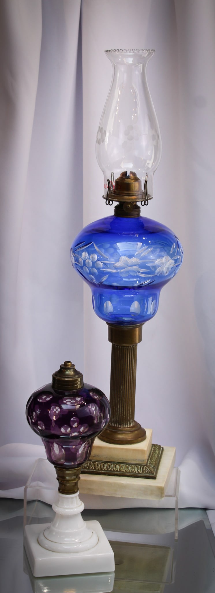 2 pc Lot Victorian Cut to Clear Stand Lamps: Select offering of two cut to clear oil lamps. One example in amythest, one in blue. Tallest measures 15".