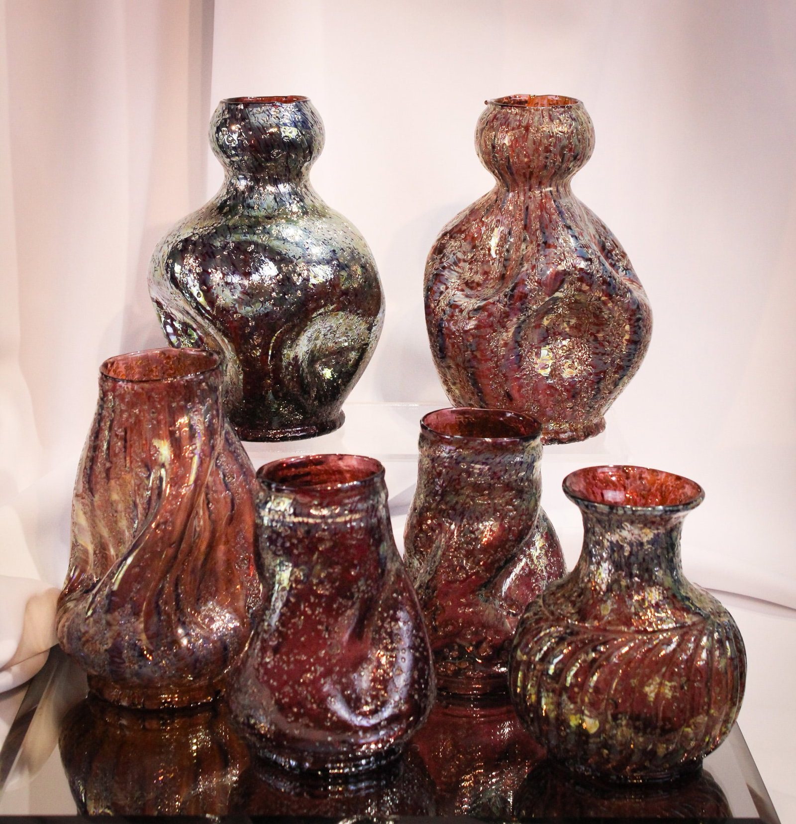 6 pc Lot Dugan Glass Pompeiian/Venetian Frit: Great examples abound in this lot of six fine examples of Dugan frit glass. Lot is comprised by examples in shades of amythest. Included is a pair of spiral swirl vases, as well as a pair of pinched s