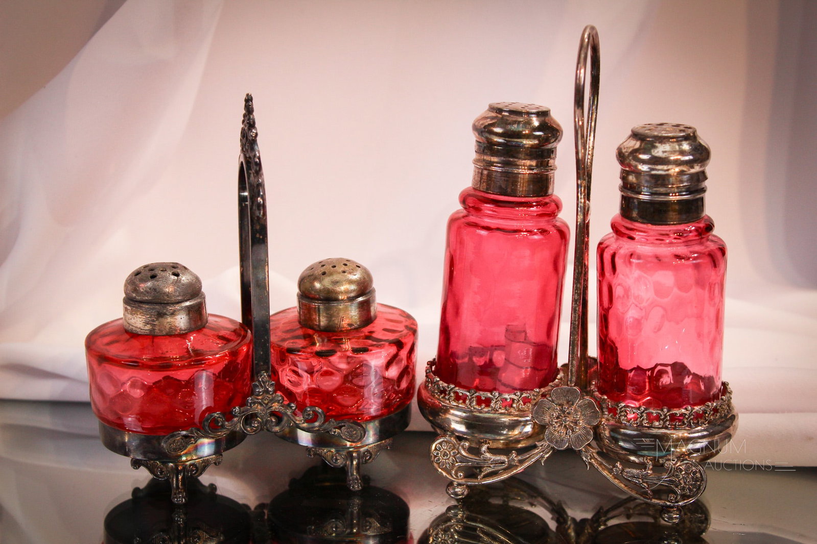 2 pc Lot Cranberry Victorian & Silverplate Shaker Sets: Two wonderful cranberry Victorian shaker pairs set in unique signed silverplate ornate holders. One stand signed Meriden silverplate. The other, Barbour. Tallest measures 6 1/2".