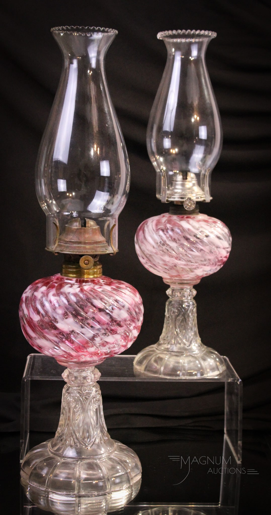 2 pc Lot Sheldon Swirl Cranberry Spatter Victorian Oil Lamps: Two fine examples of Sheldon Swirl in Cranberry spatter Victorian glass stand lamps. One stands 9" and the other 7" for the glass portion only. Rich cranberry spatter glass fonts with clear bases.