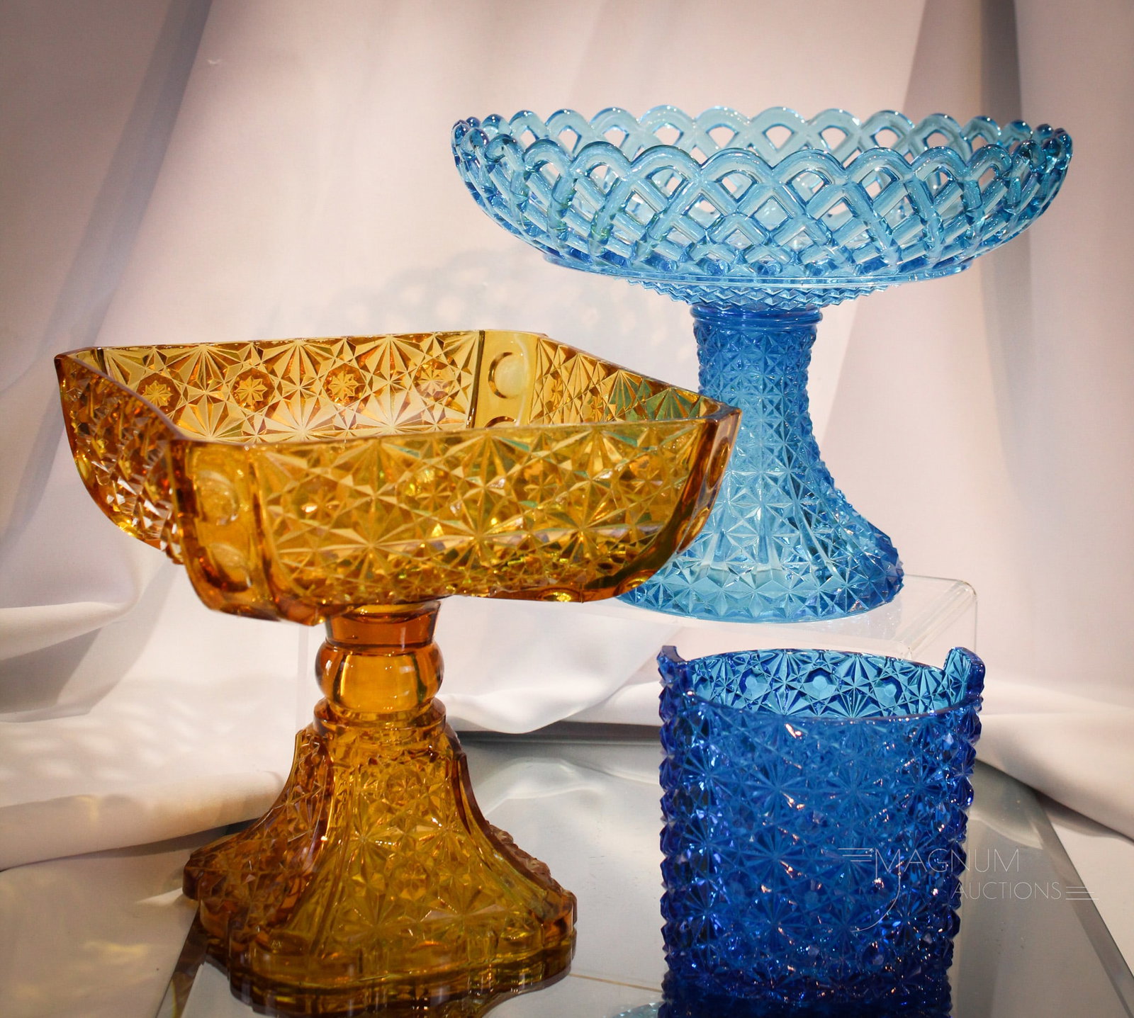 3 pc Lot Victorian Pattern Glass Compotes & More: Three fun pieces of Victorian colored pattern glass comprised of an amber compote, a blue lattice pattern compote, along with a blue Daisy & Button piece. Largest measures 7 1/2" tall.