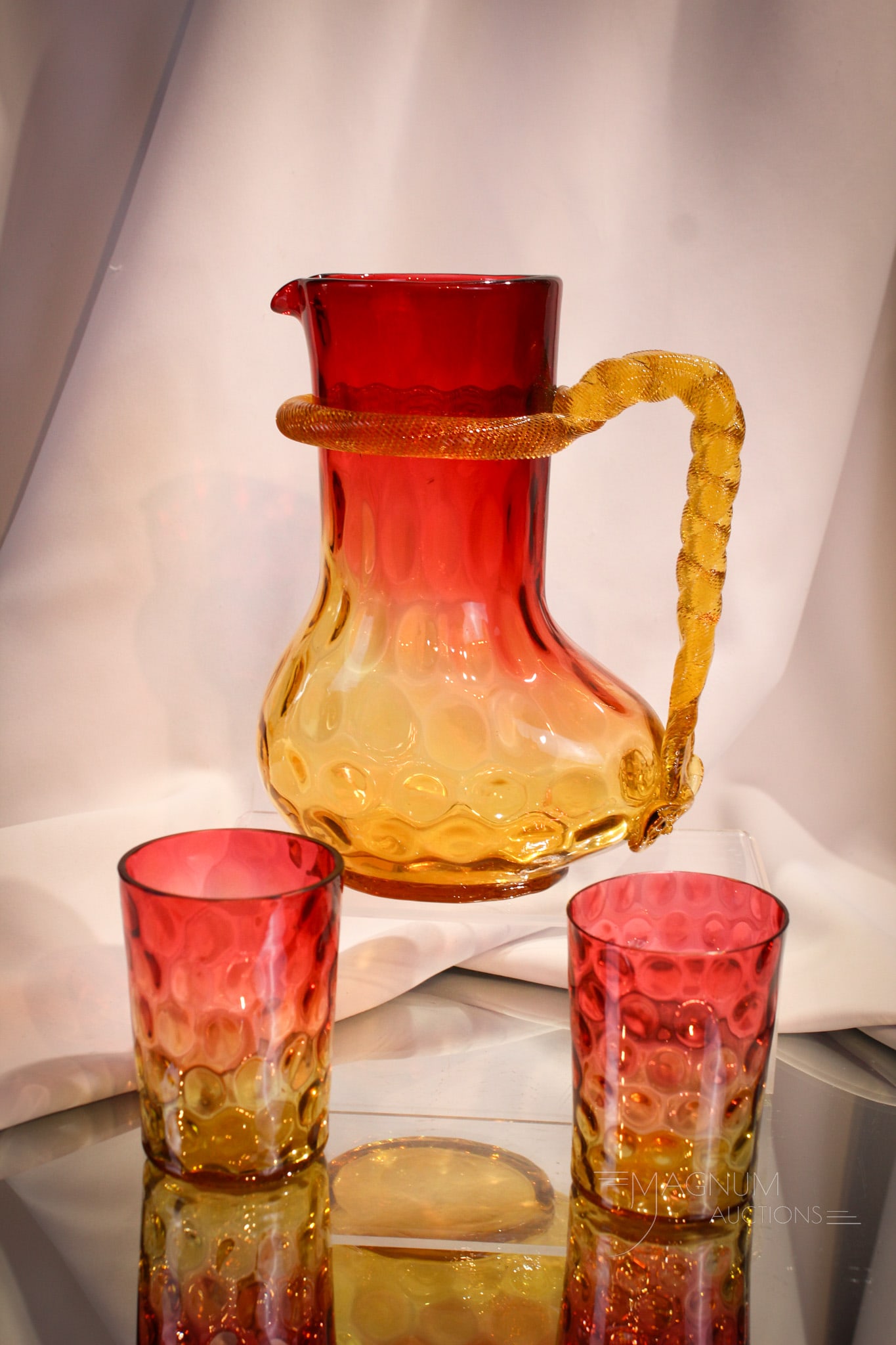 3 pc Lot Amberina Rope Handle Pitcher & Tumblers: Quite the unusual form for a pitcher. This one with a big booty. Applied rope handle around the neck makes this a stand out piece. Pitcher is offered with two tumblers. Tallest measures 8 1/2".