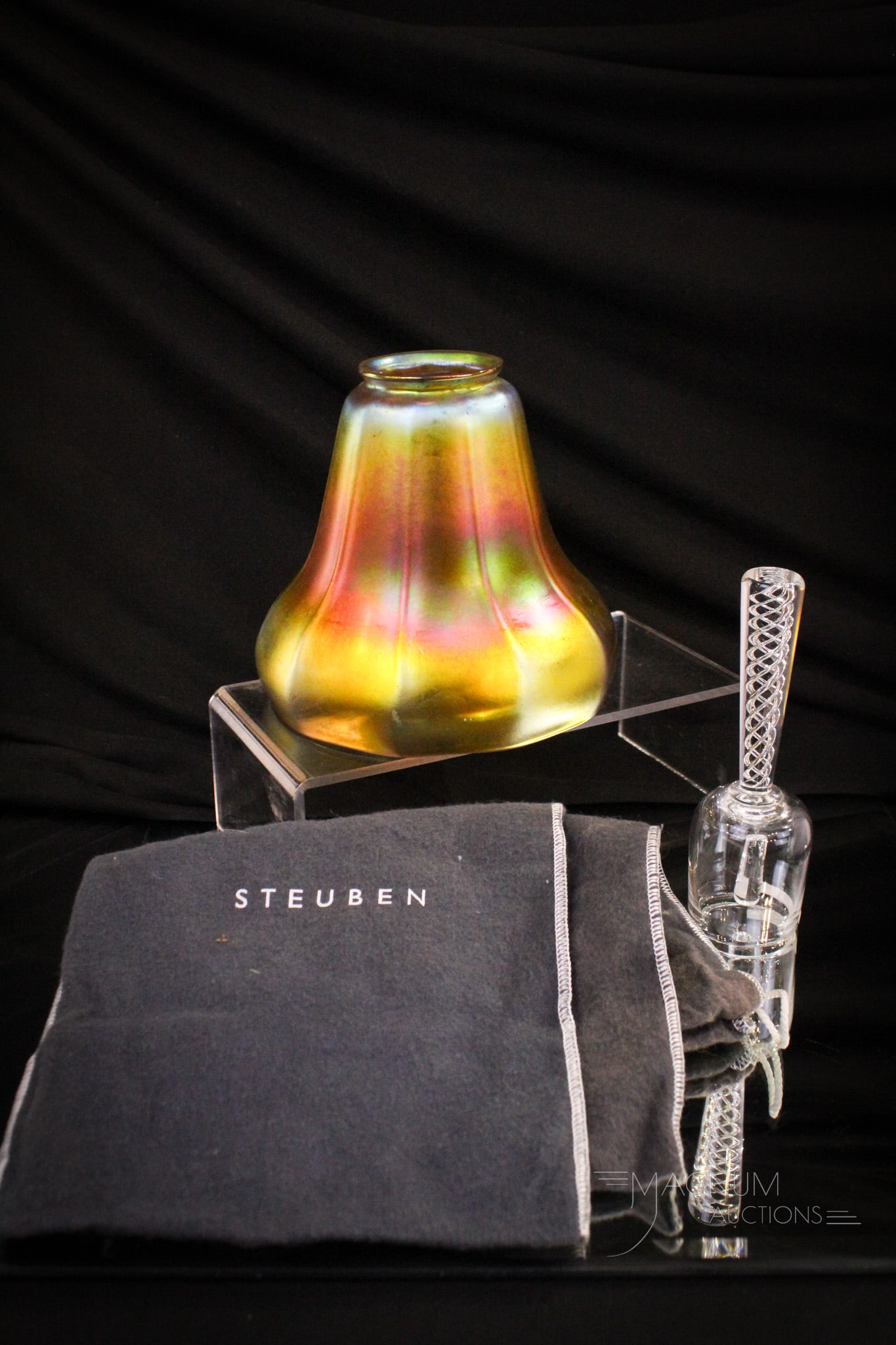 4 pc Lot Steuben Gold Aurene Shade & More: Generous offering in this four piece lot of Steuben glass and more. Lot is comprised of a gold aurene shade. A signed Steuben clear bell. Lot is completed by two flannel bags marked Steuben. Largest m
