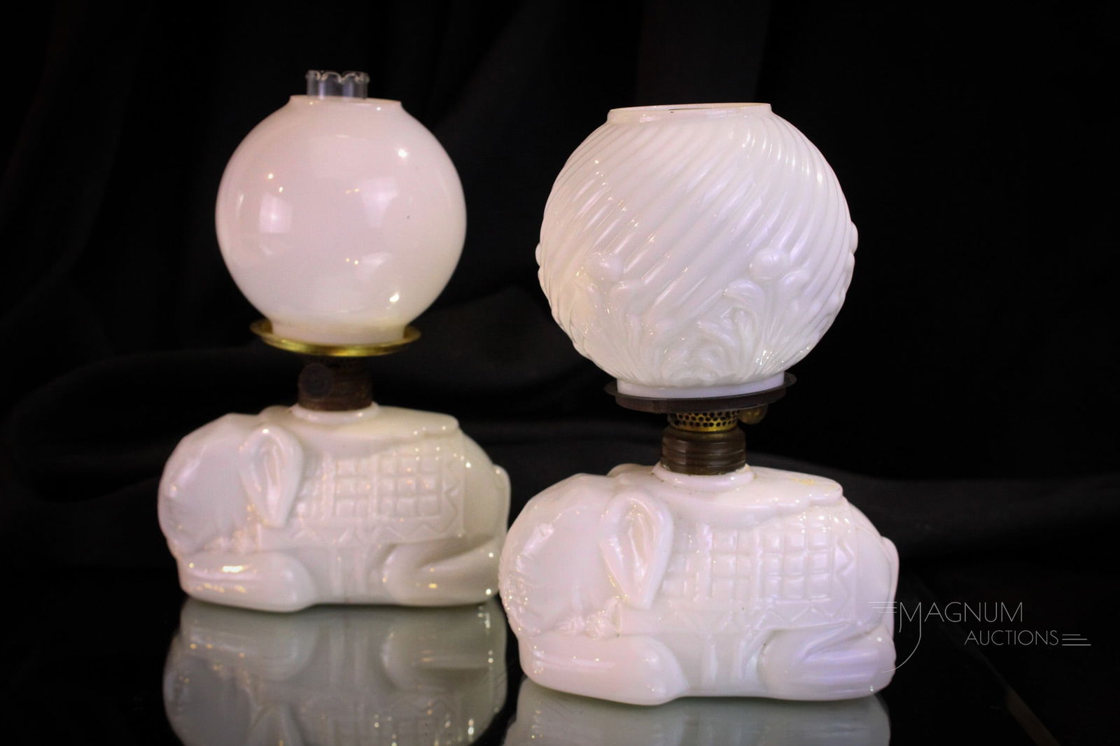 2 pc Lot Victorian Miniature Milk Glass Elephant Oil Lamps: Two fine examples of a reclining elephant Victorian miniature oil lamp. Each lamp with unique shade and chimney. One shade is correct. This one exhibits a chip as shown at the fitter end. The other wi