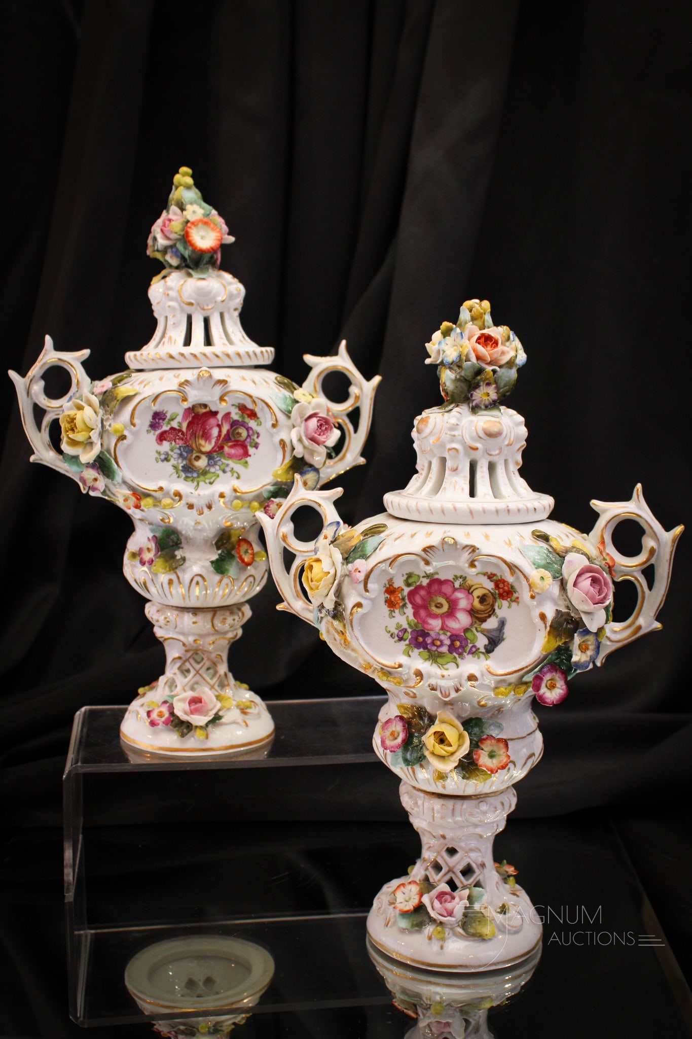 Meissen Style Porcelain Mantle Urns: Fine offering of a pair of Meissen-style porcelain mantle urns complete with lids. Each piece adorned with applied decorations. Each urn measuring 11" tall. Losses to applied decoration on each.