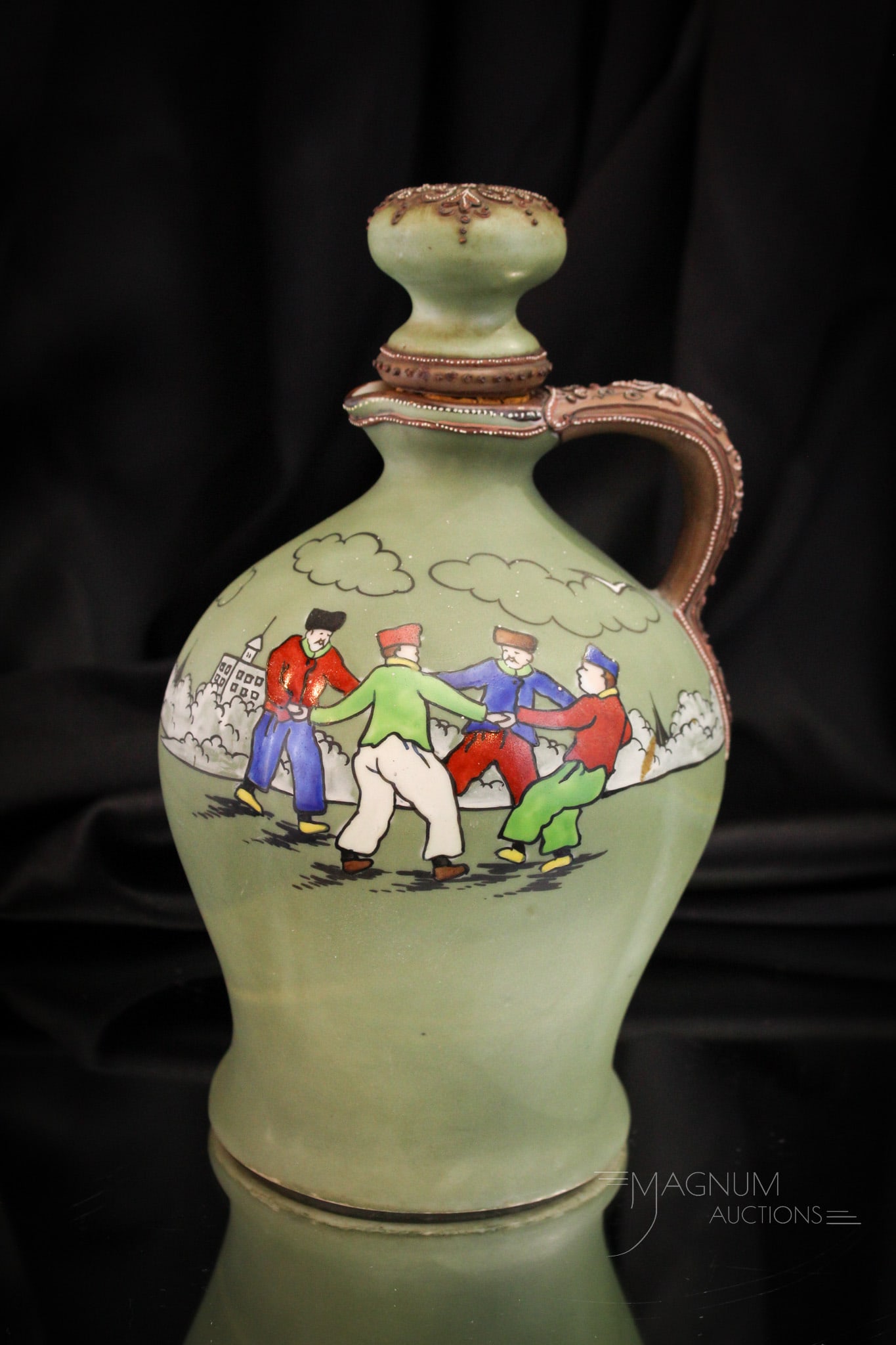 Marked Nippon Porcelain Whisky Jug: Select offering of a marked Nippon whisky jug. Piece is decorated with frolicking men holding hands in a circle. Jug is complete with the original stopper. Jug measures 9 1/2" tall.