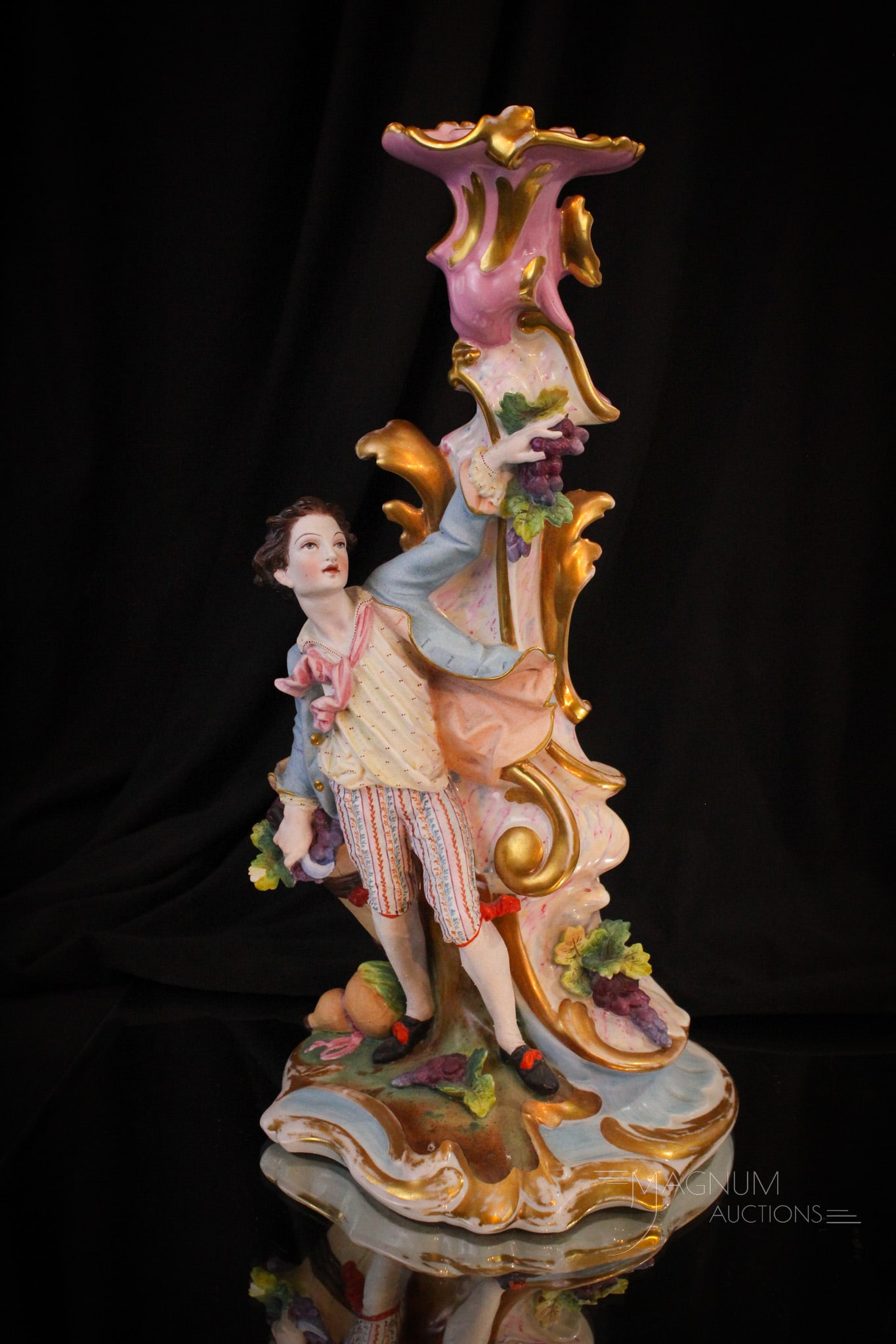 Victorian Porcelain Figural Candlestick: Finely detailed Victorian porcelain candlstick featuring figure in period Georgian attire. Piece adorned with grapes.. Measures 13 1/2" tall.