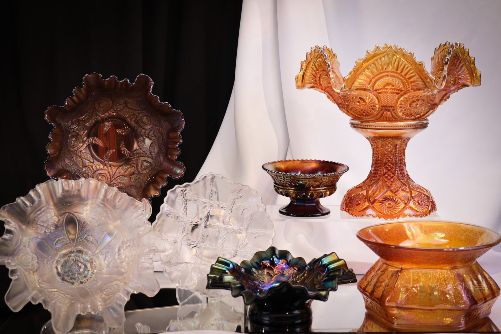 7 pc Lot Carnival Glass Northwood Fenton Dugan & More: Selections abound in this lot of seven pieces of antique carnival glass. This lot includes a purple Grape and Cable with Thumbprint sherbert, a white Apple Blossom Twigs bowl, an electric purple bowl 