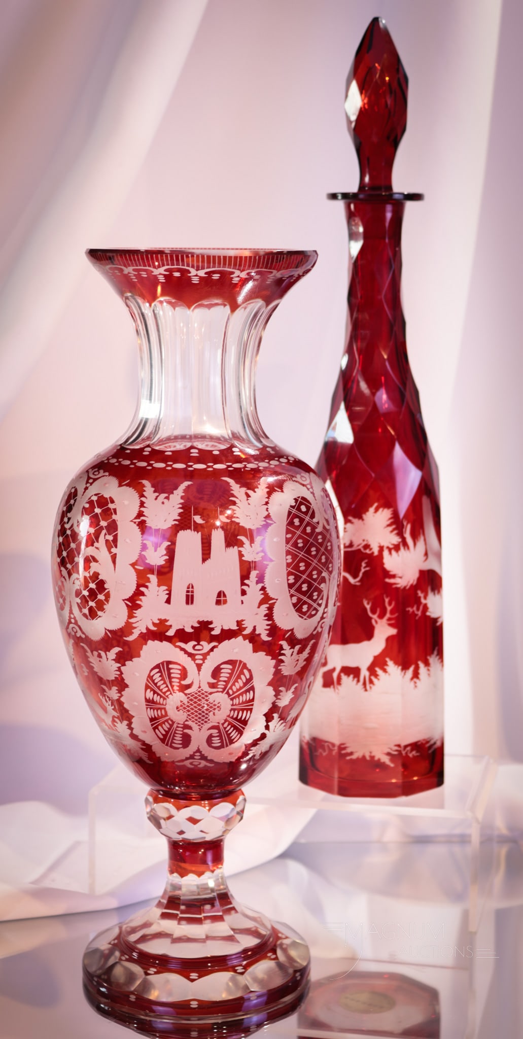2 pc Lot Ruby Stained Cut Engraved Glass Cologne & Vase: Fine offering of two lovelies in cut and engraved ruby stained glass in the form of a cologne bottle and vase. Cologne bottle with original stopper. Both decorated with deer motif. Tallest measures 16