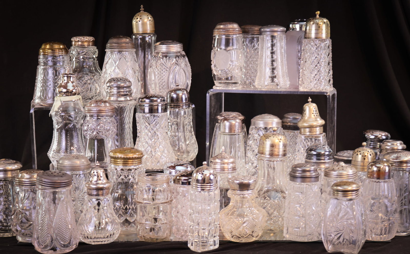 43 pc Mega Magnum Auctions Lot Clear Glass Sugar Shakers: Mega Magnum Auctions lot of 43 unique clear glass sugar shakers. Various ages and manufacturers and mediums. Some pressed glass. Some cut glass. Some with sterling lids. Tallest measures 7 1/4".