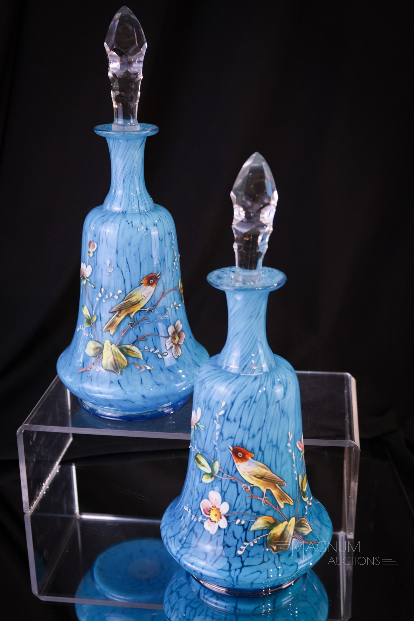 Pair Victorian Blue Cased Spatter Glass Cologne Bottles: A beautiful pair of Victorian opposing decoration Victorian cologne bottles in blue cased spatter glass. Each is enameled with birds and flowers with gilt highlights. Each with curvacious form. Both m