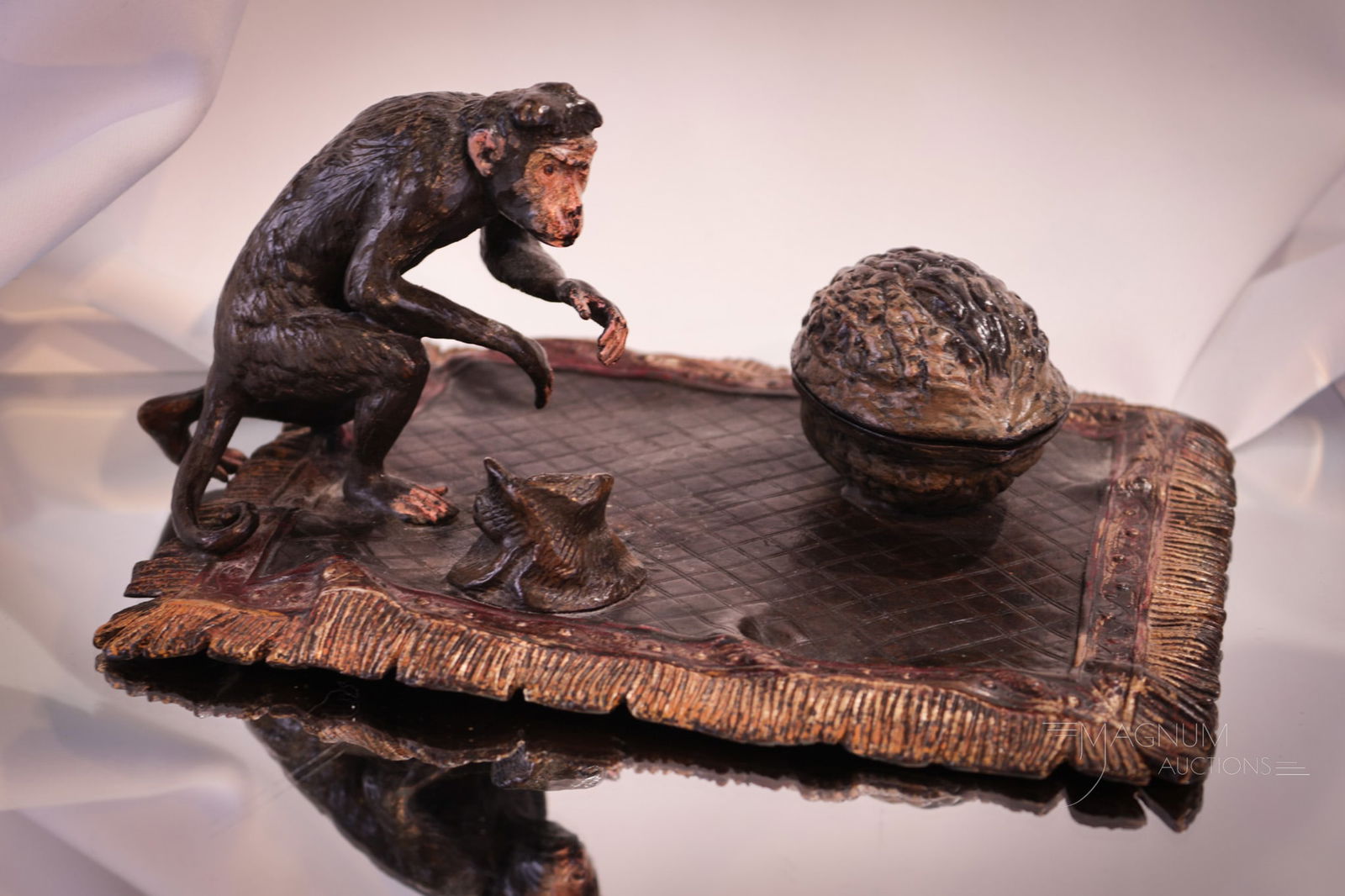 Cold-painted Geschutzt Bronze Monkey on Oriental Rug Inkwell: Charming cold-painted Bronze inkwell in the form of a monkey on an oriental rug with a nut. Piece is signed Geschutzt. Glass inkwell insert is present. Piece measures 3 1/2" tall, 8 1/2" wide.