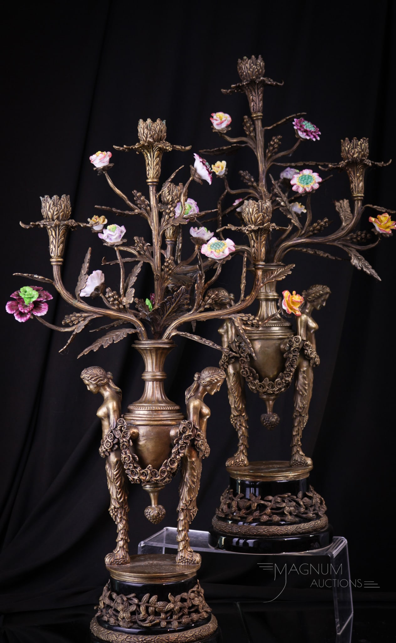 Pair of 24" Figural Bronze& Porcelain Candleabrum: Fine pair of figural caryatid adorned bronze candlabrum with porcelain flowers and pottery bases. Each candleabrum measures 24" tall. Both retain original patina. Some losses are noted to porcelain fl
