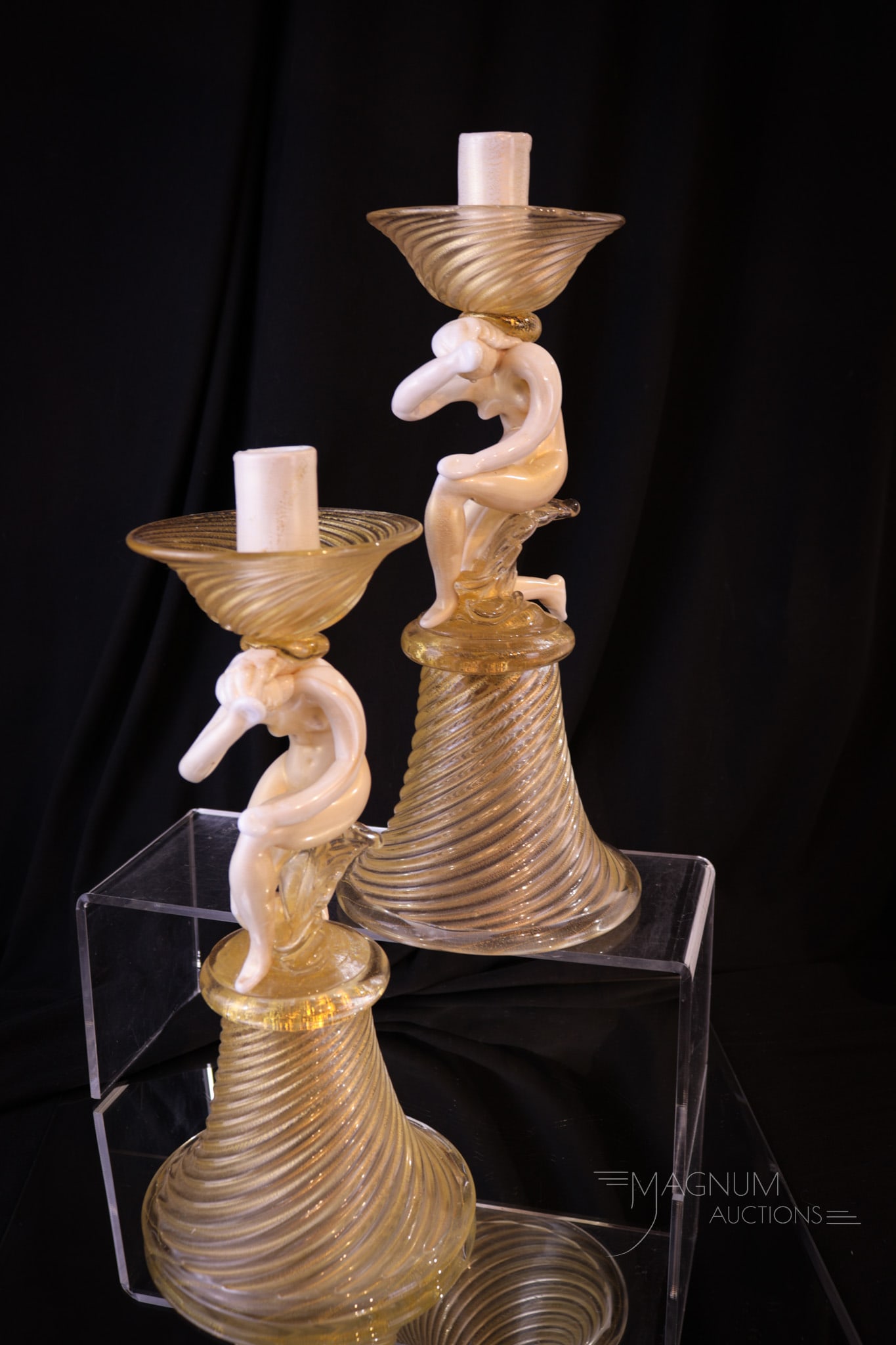 Pair Italian Murano Nude Figural Candlesticks: Fine pair of unusual Italian Murano art glass figural candlesticks featuring a female nude on each. Each with a swirl mold and gold flecks. Each measures 11 1/2" tall.
