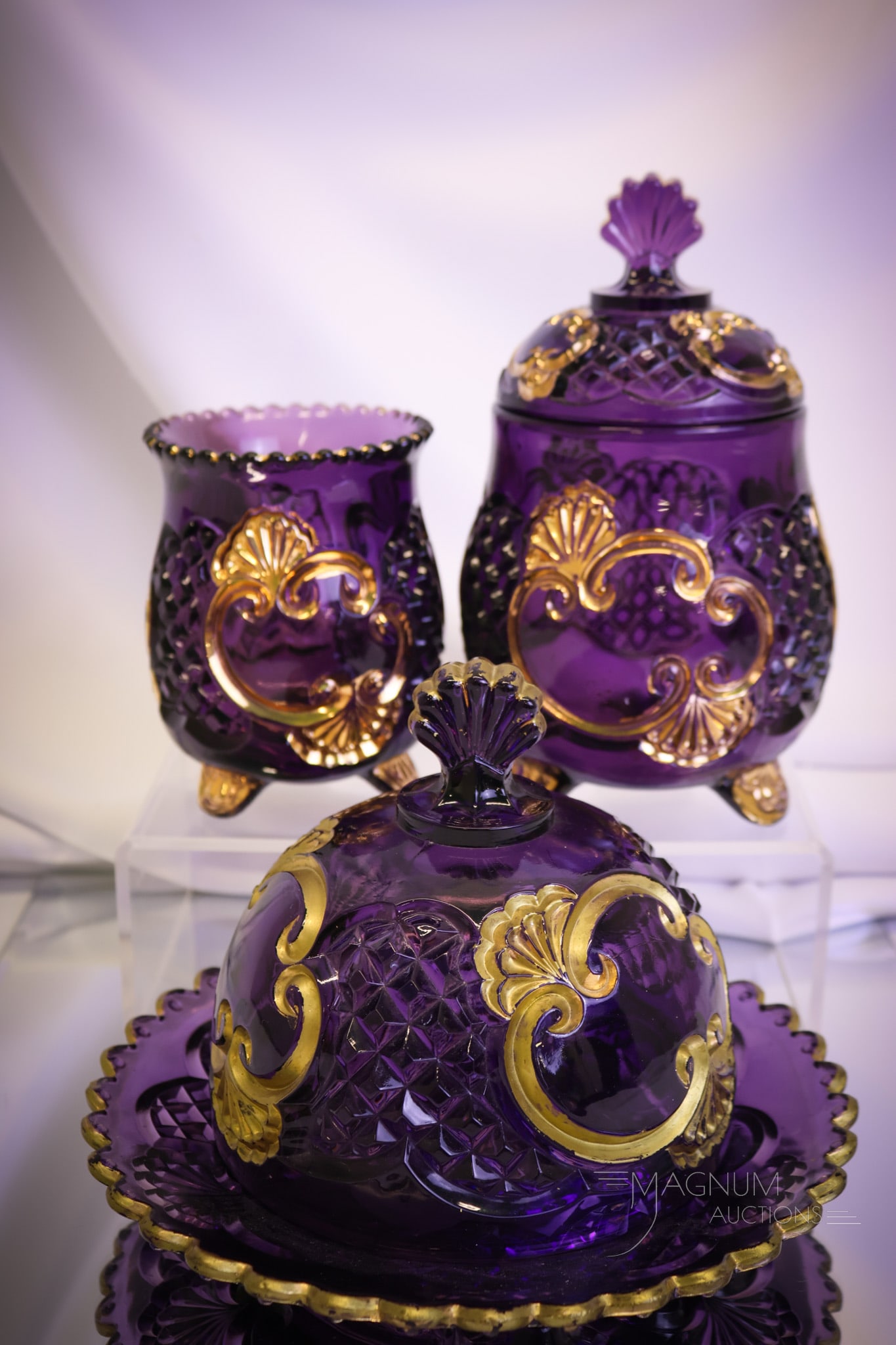 3 pc Lot Victorian Riverside Amethyst Croesus Glass: Three unique items in Victorian Riverside Croesus glass. This lot offers a covered butter, a covered sugar, and a spooner. The largest of the offering measures 7 1/2"" tall and 8"" wide. There appears