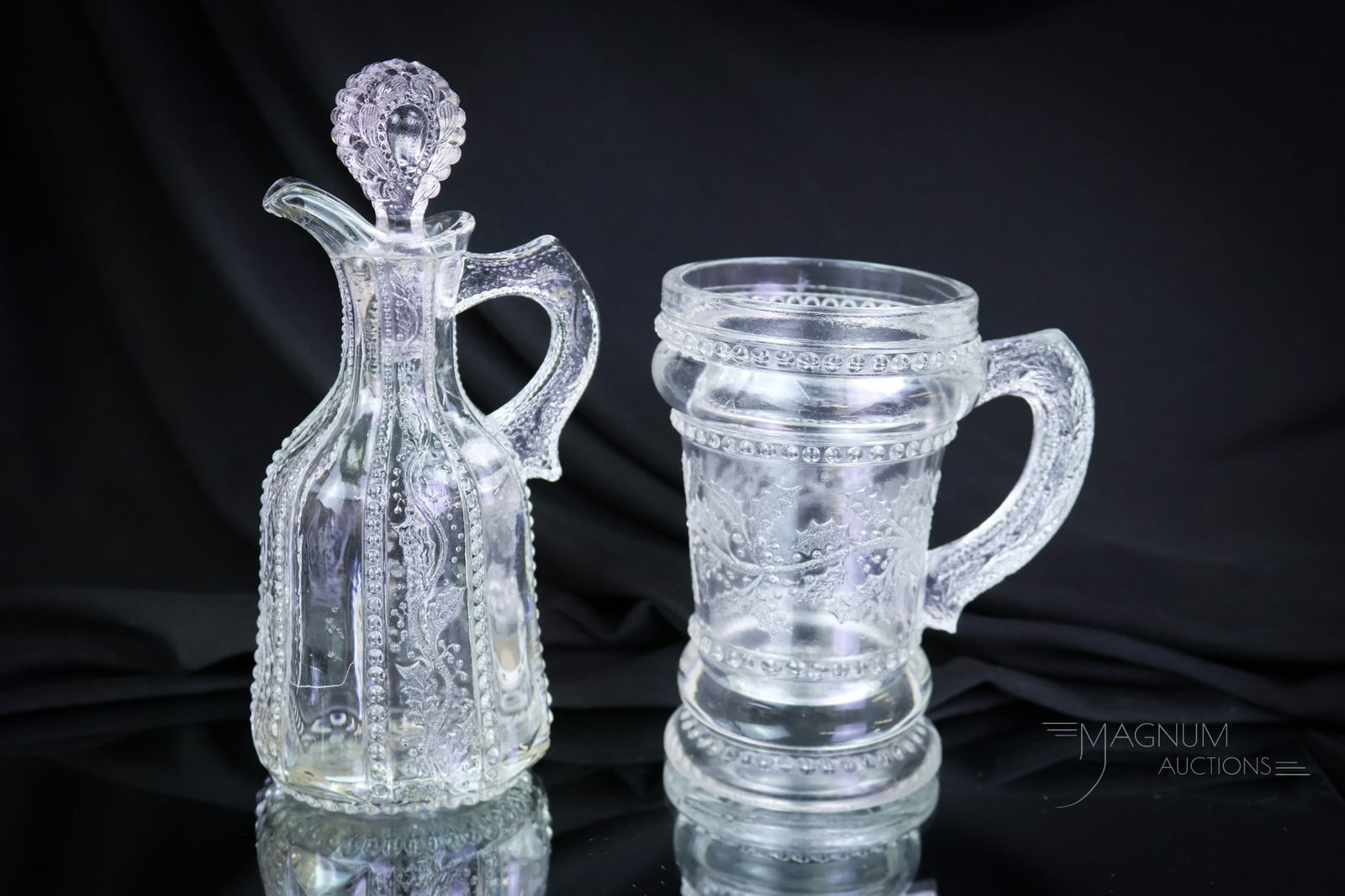 2 pc Lot Greentown Victorian Glass Holly Cruet & Mug: Two highly collectible examples of Greentown Victorian clear Holly pattern. This lot includes a cruet and a mug. The tallest measures 6 1/2". SHIPPING NOTICE: If you choose not to utilize the LiveAuct