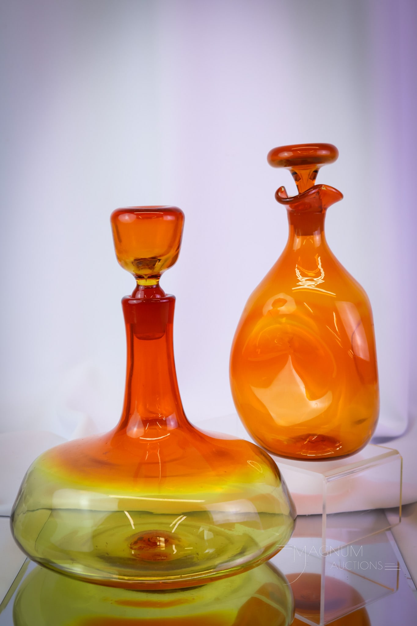 2 pc Lot Blenko MCM Art Glass Decanters: Two superb examples of fine Blenko art glass decanters in orange and tangerine amberina coloring. The orange is numbered #49. The tangerine amberina is numbered #565. The tallest measures 10 3/4" tall
