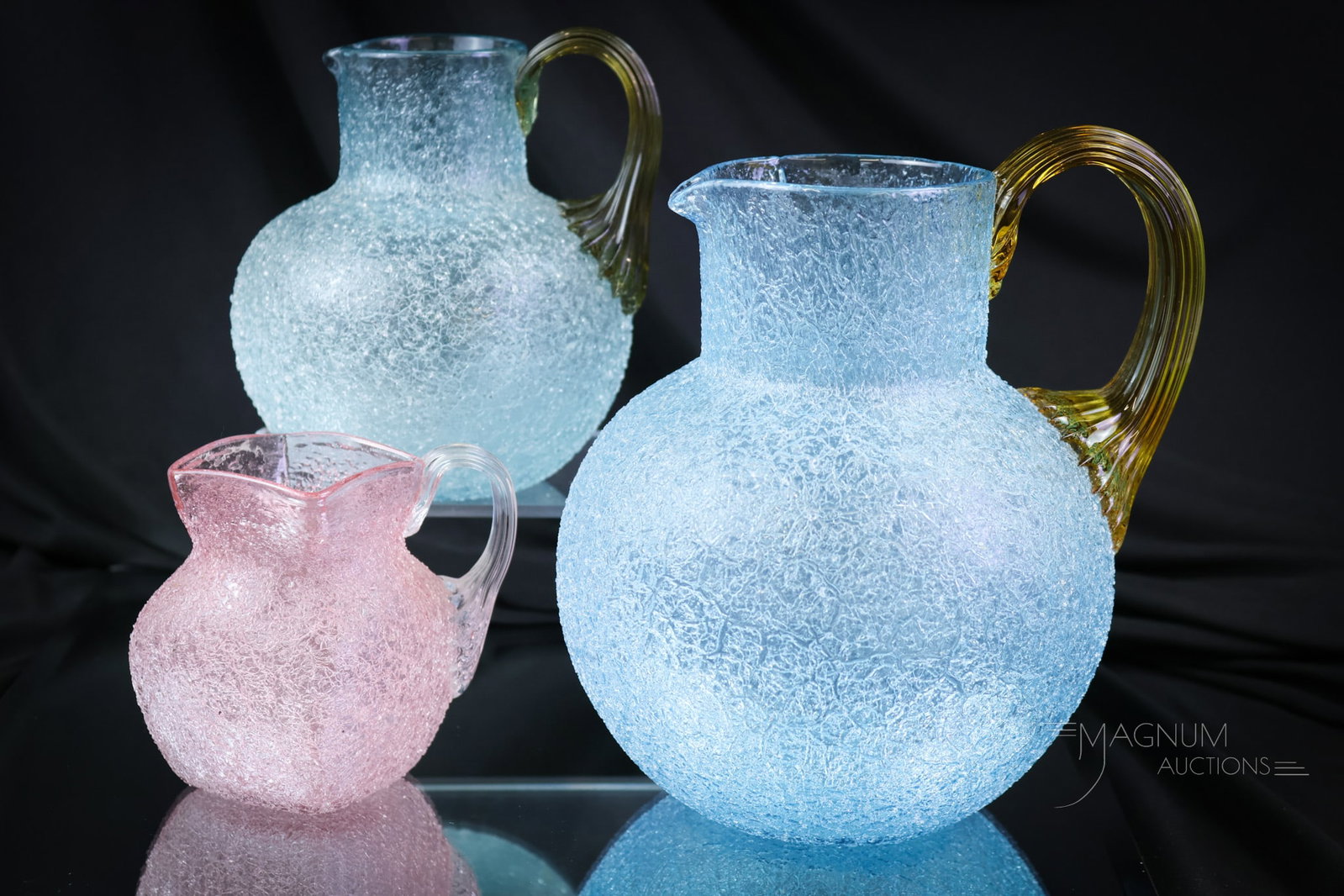 3 pc Lot Victorian Overshot Glass Pitchers: Three super examples of colorful overshot Victorian art glass pitchers. There is a blue with an amber handle water pitcher. The next is the same color but in a milk pitcher size. The third is a pink w
