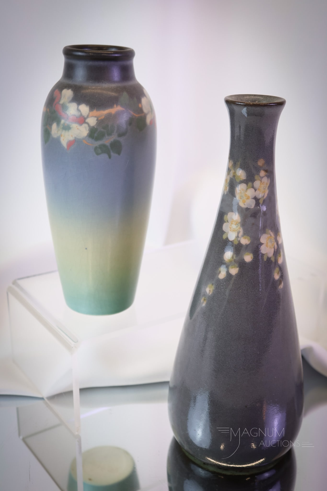 2 pc Rookwood Vellum Glaze Floral Decorated Vases: two desirable finds in Rookwood Vellum glaze vases with floral decoration. The first is blue in color. It is numbered "918E & XX." The second is a blue-grey color. It is numbered, "1872 & XX." The tal