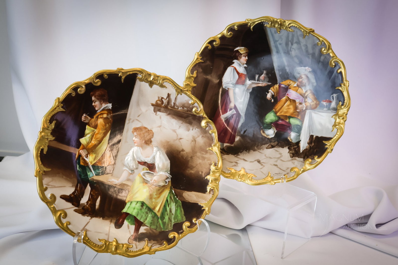 2 pc Lot Limoges Dubois Hand Painted Porcelain Chargers Plaques: This lot offers a pair of LimogesFrance plaques. Each is abundantly decorated with gold. One depicts a drinking man and a female. The other has a couple. Each piece is signed, "Dubois." The largest me