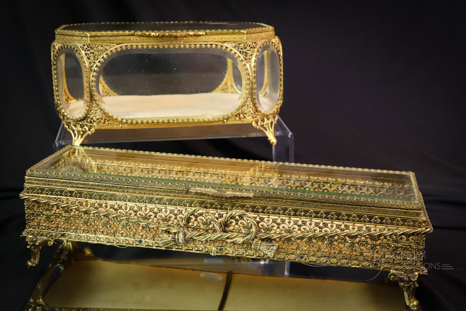 2 pc Lot Hollywood Regency Brass & Beveled Glass Jewelry Caskets: Two wonderful fids in Hollywood Regency jewelry caskets. Each of these decorative pieces features beveled glass and ornate brass trim. Each has a cushion tufted lining. The tallest measures 5". SHIPPI