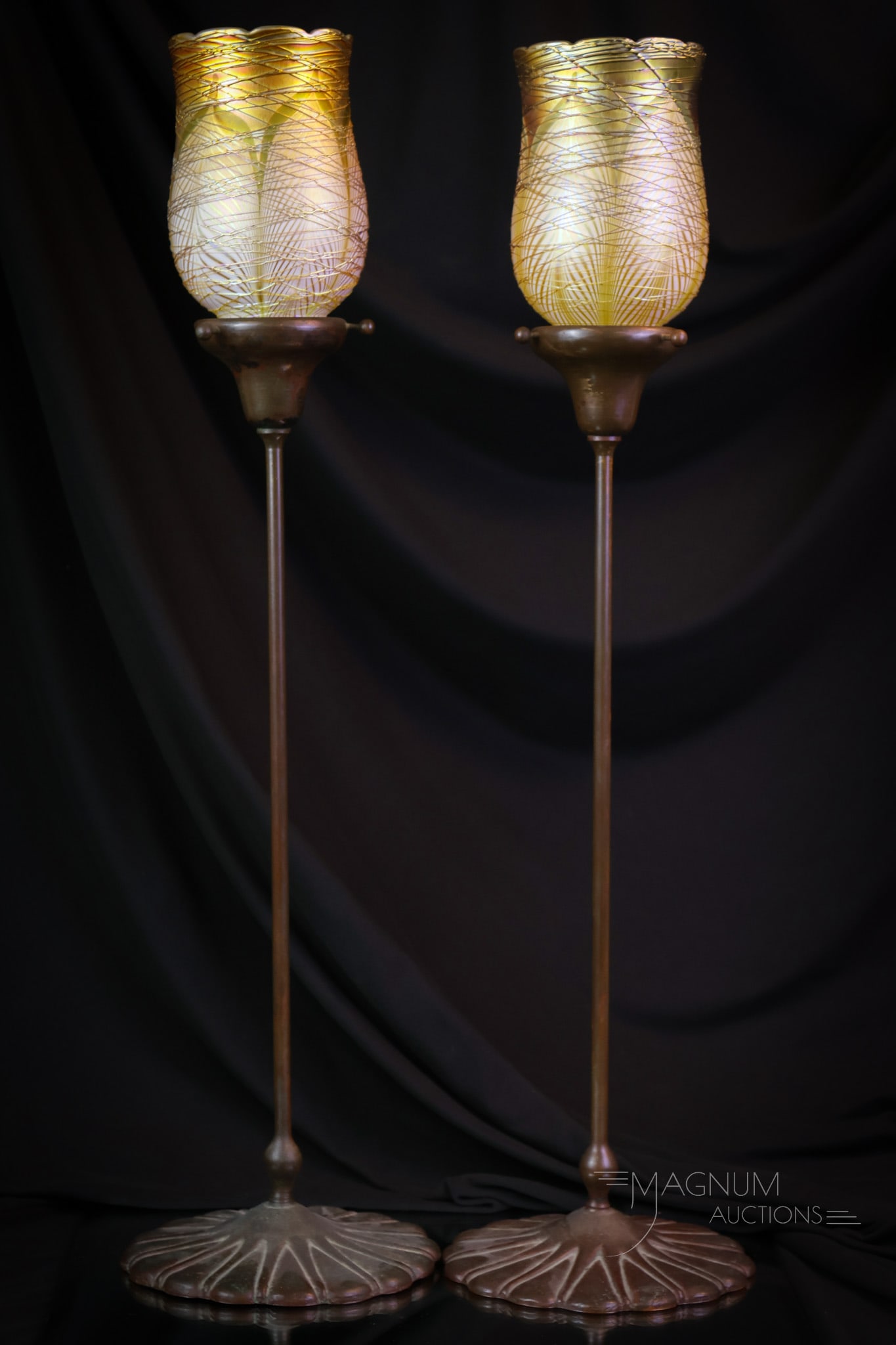 Pair of Lustre Art Pulled Feather Art Glass & Bronze Candle Lamps: A beautiful pair of marked bronze candlesticks with a pair of Lustre Art iridescent threaded glass shades. The base of each candle holder is marked with an impressed mark. Each of the shades is signed